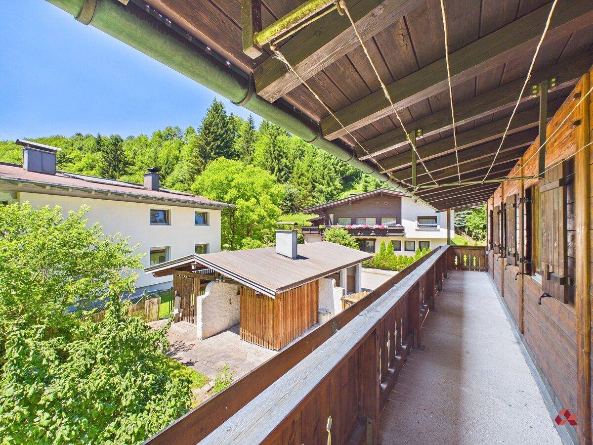 Langer Holzbalkon mit Blick auf benachbarte Häuser und die bewaldete Umgebung.