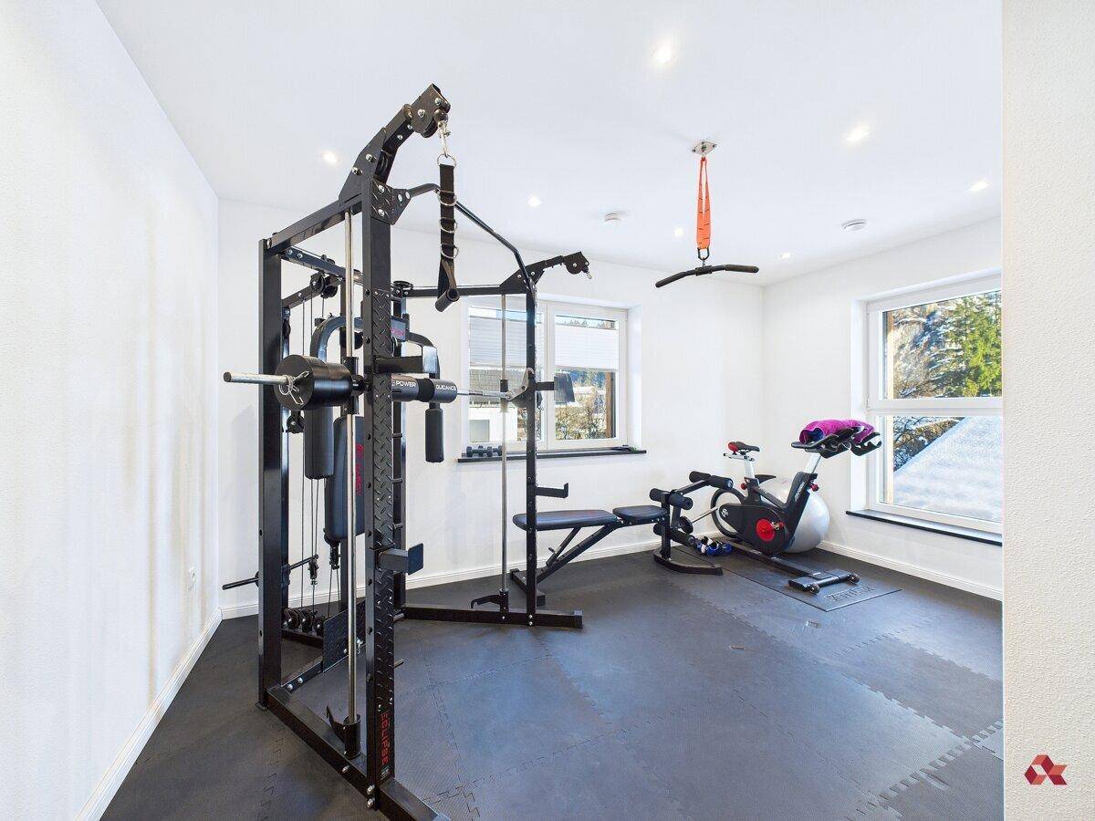 Geräumiger Fitnessraum mit verschiedenen Trainingsgeräten und Fenstern für Tageslicht.