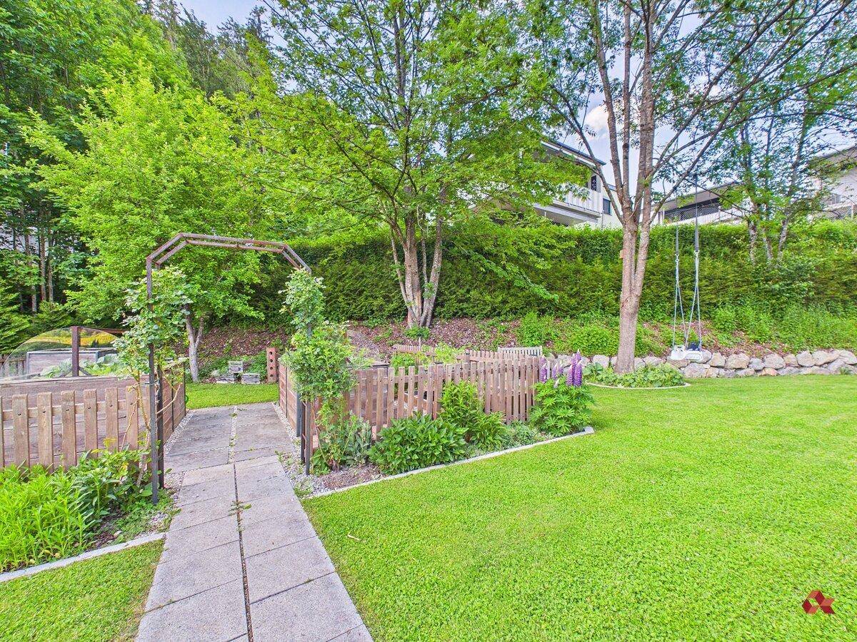 Gartenbereich mit einem gepflasterten Weg, umgeben von Hecken und Bäumen.