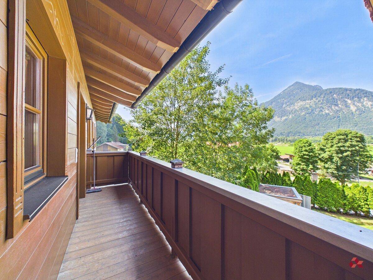 Langer Holzbalkon mit Bergblick und grüner Umgebung, ideal zum Entspannen.