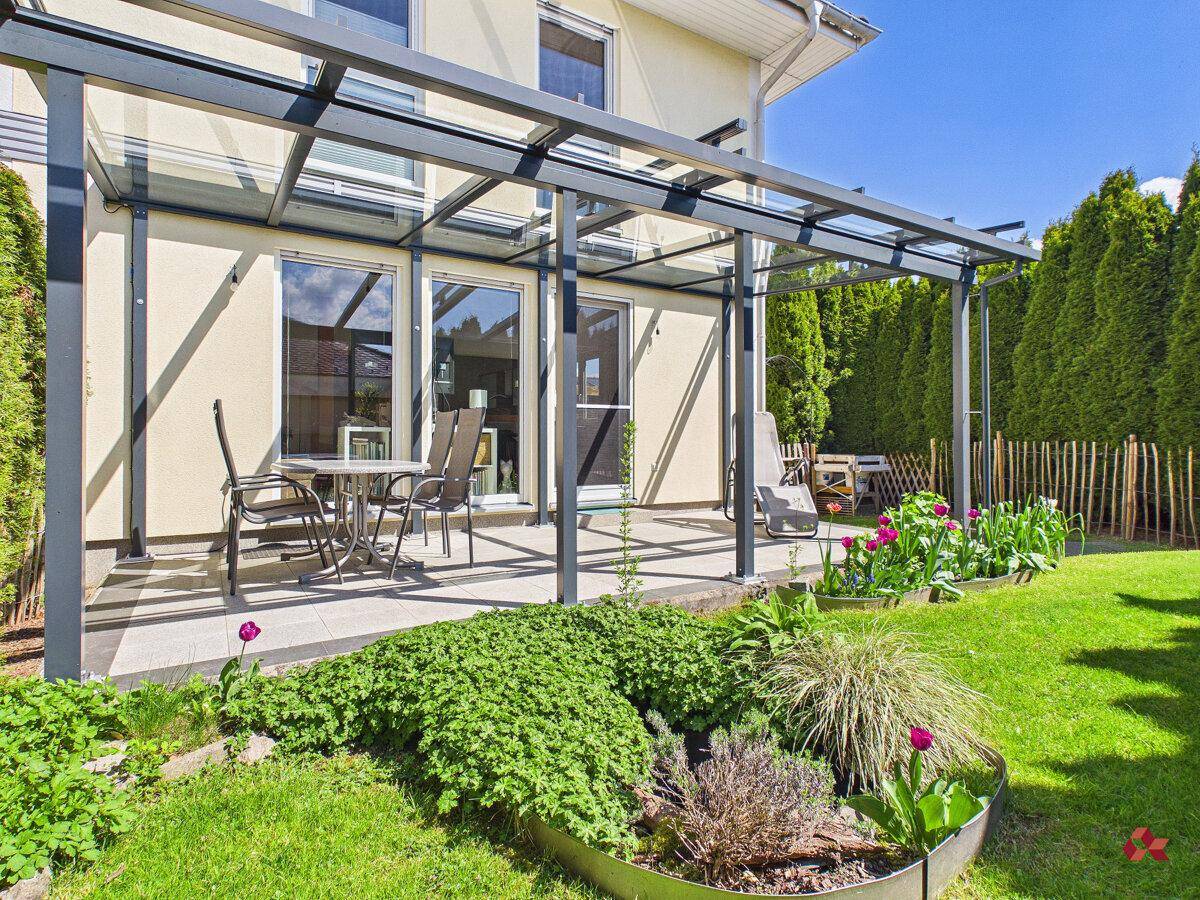 Sonnige, überdachte Terrasse mit Gartenmöbeln und gepflegter Rasenfläche.