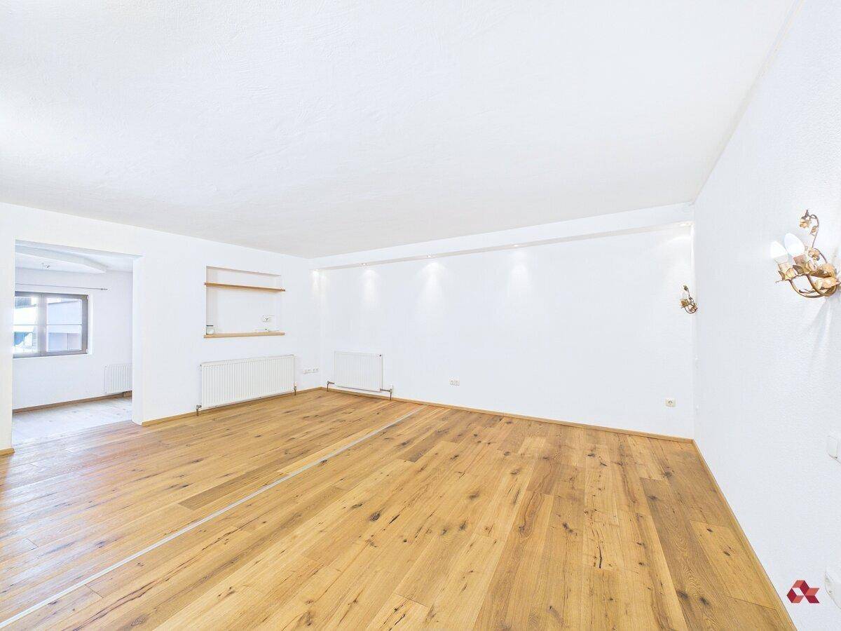 Helles, leeres Wohnzimmer mit neuem Holzboden und weißen Wänden, bereit zur Einrichtung.