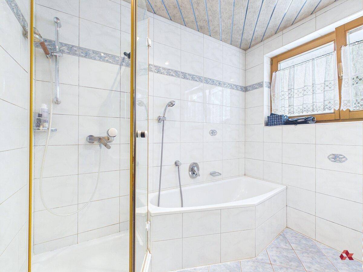 Badezimmer mit weißen Fliesen, Eckbadewanne und Duschkabine sowie einem Fenster.