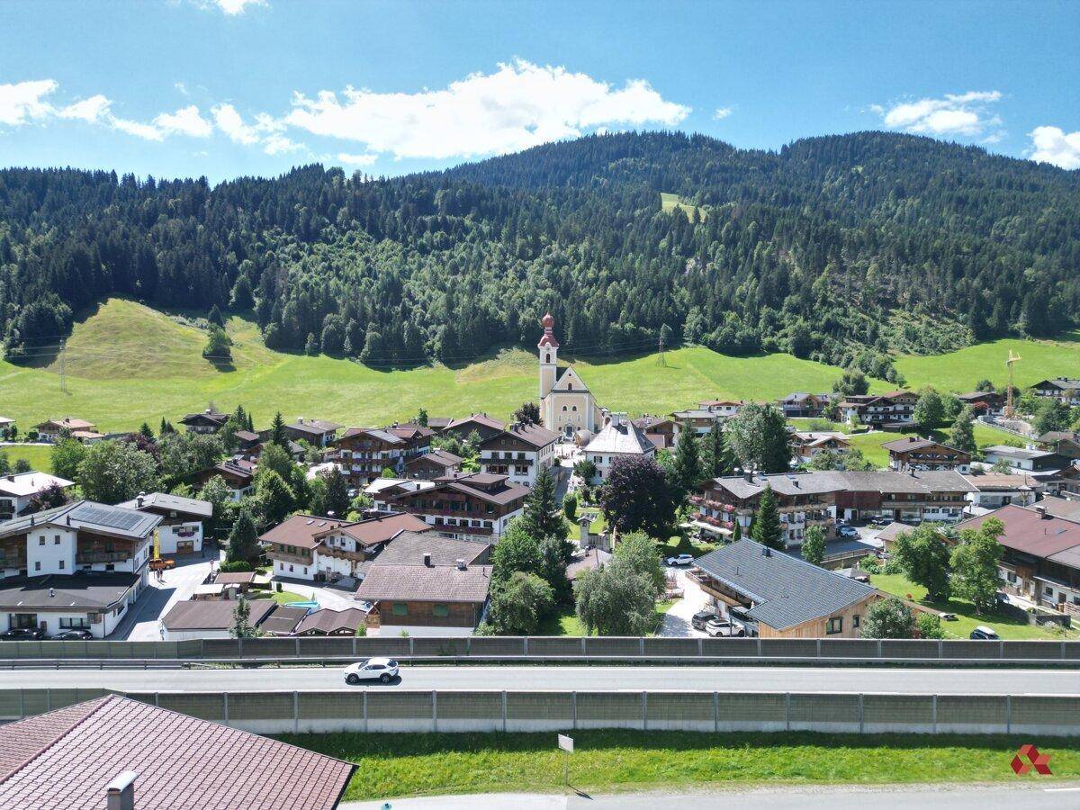 Luftaufnahme eines charmanten Dorfes mit Kirche, umgeben von Wäldern und Bergen.