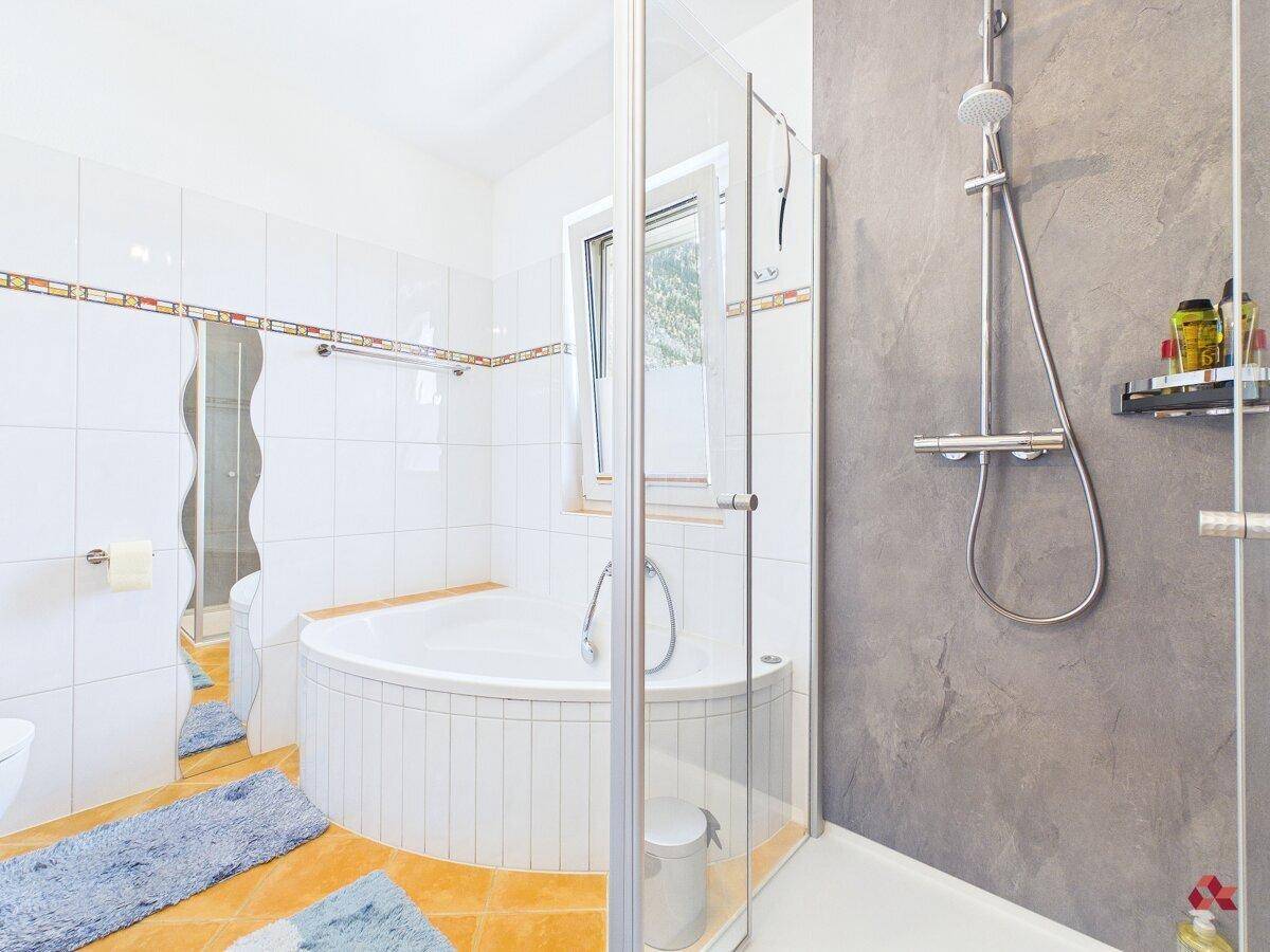 Badezimmer mit Eckbadewanne, separater Dusche und Fenster.