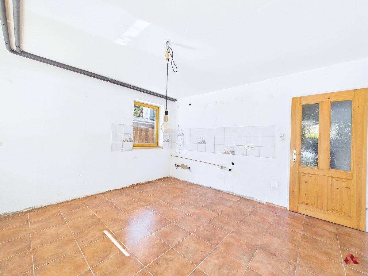 Leerer Küchenraum mit Fliesenboden, Fenster und vorbereiteten Anschlüssen.