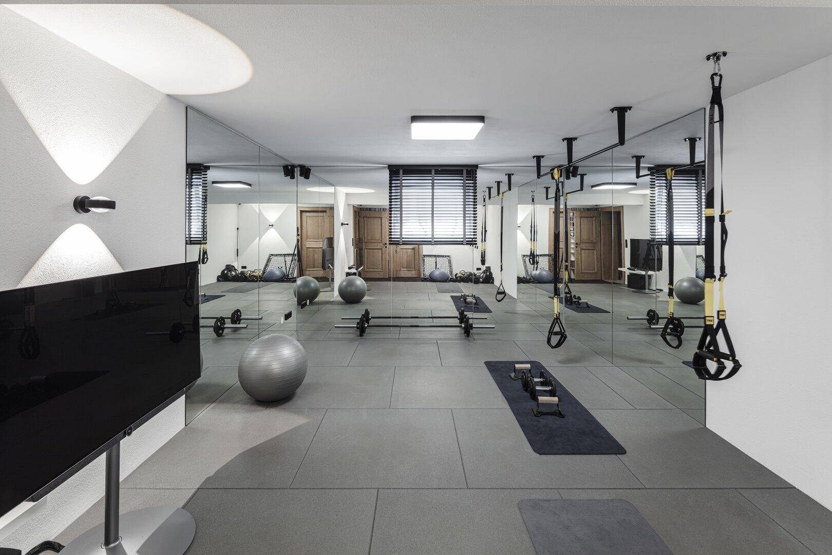 Moderner Fitnessraum mit Spiegelwänden, Trainingsgeräten und hellem Boden.