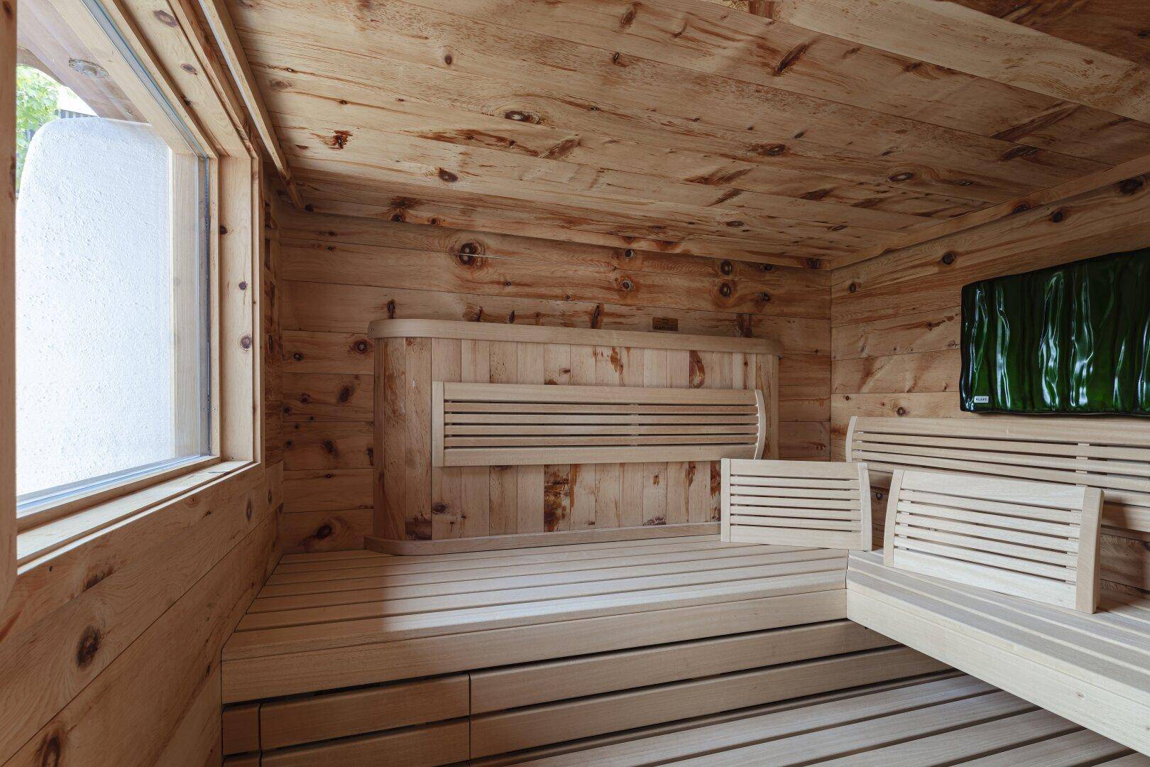 Geräumige Holzsauna mit bequemen Bänken und einem Fenster für natürliches Licht.
