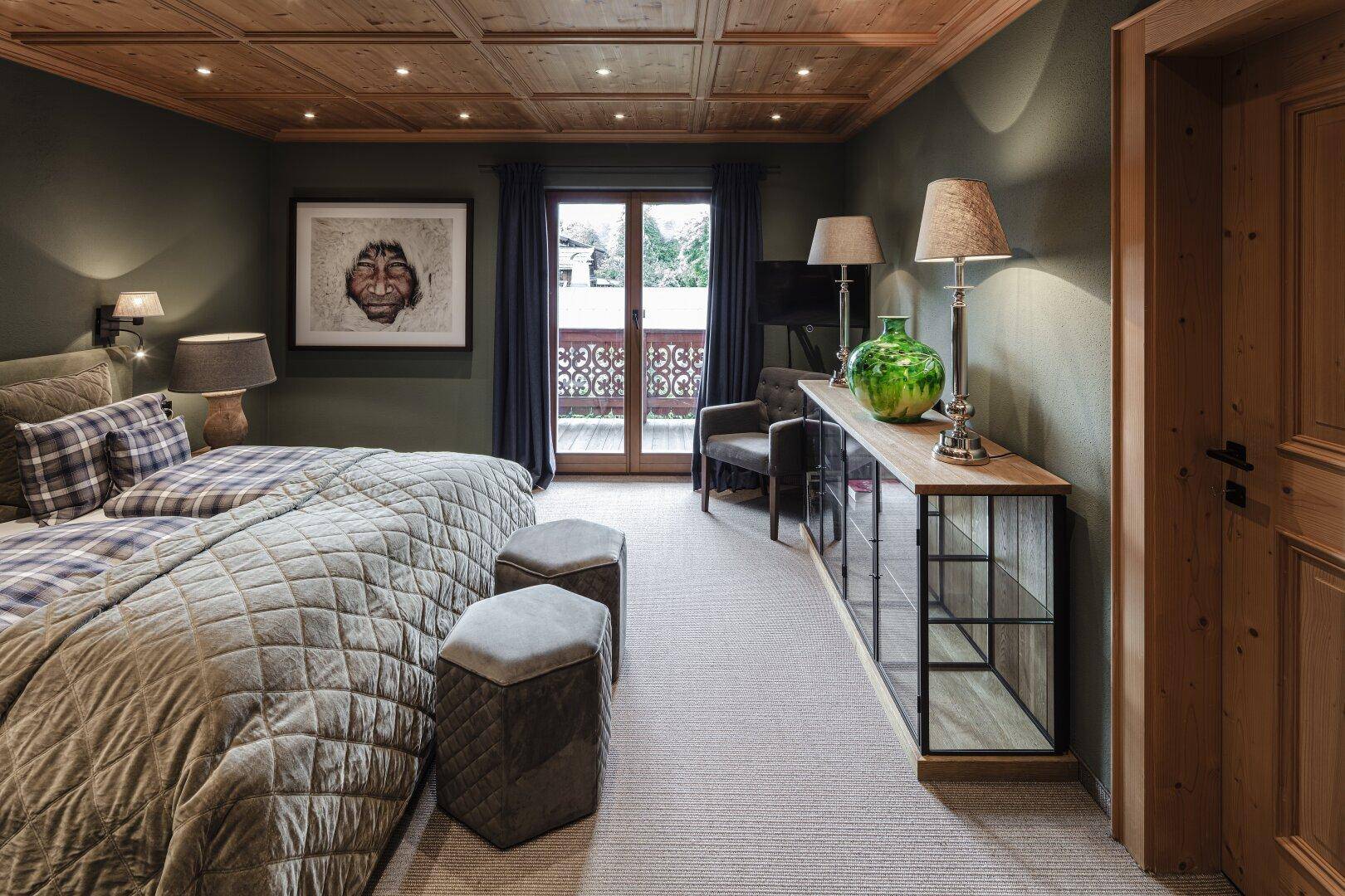 Helles Schlafzimmer mit Holzbalkendecke, Teppichboden und Zugang zu einem Balkon.