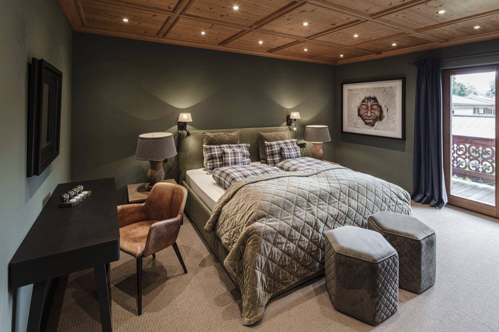 Gemütliches Schlafzimmer mit Holzbalkendecke, Teppichboden und Balkonzugang.