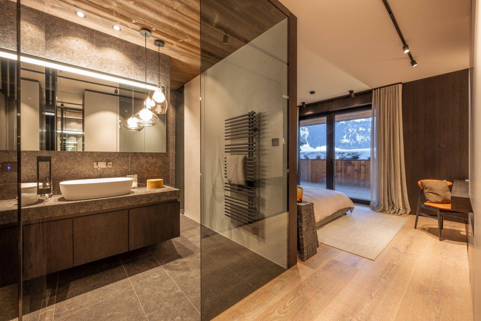 Stilvolles Badezimmer mit Einzelwaschbecken, beheiztem Handtuchhalter und Blick ins Schlafzimmer mit Balkon.