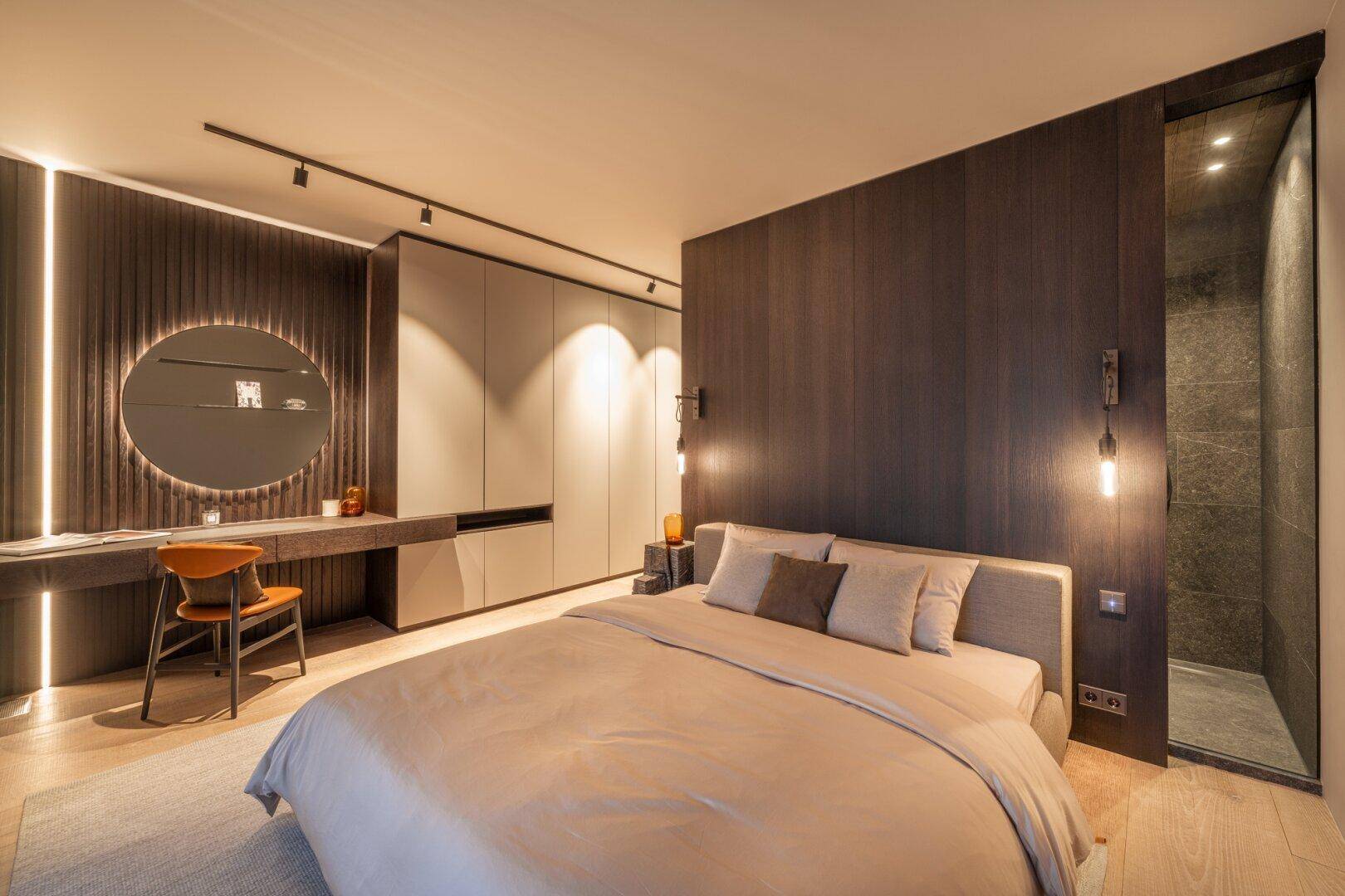Modernes Schlafzimmer mit integrierten Schränken, Schminktisch und offener Duschkabine.