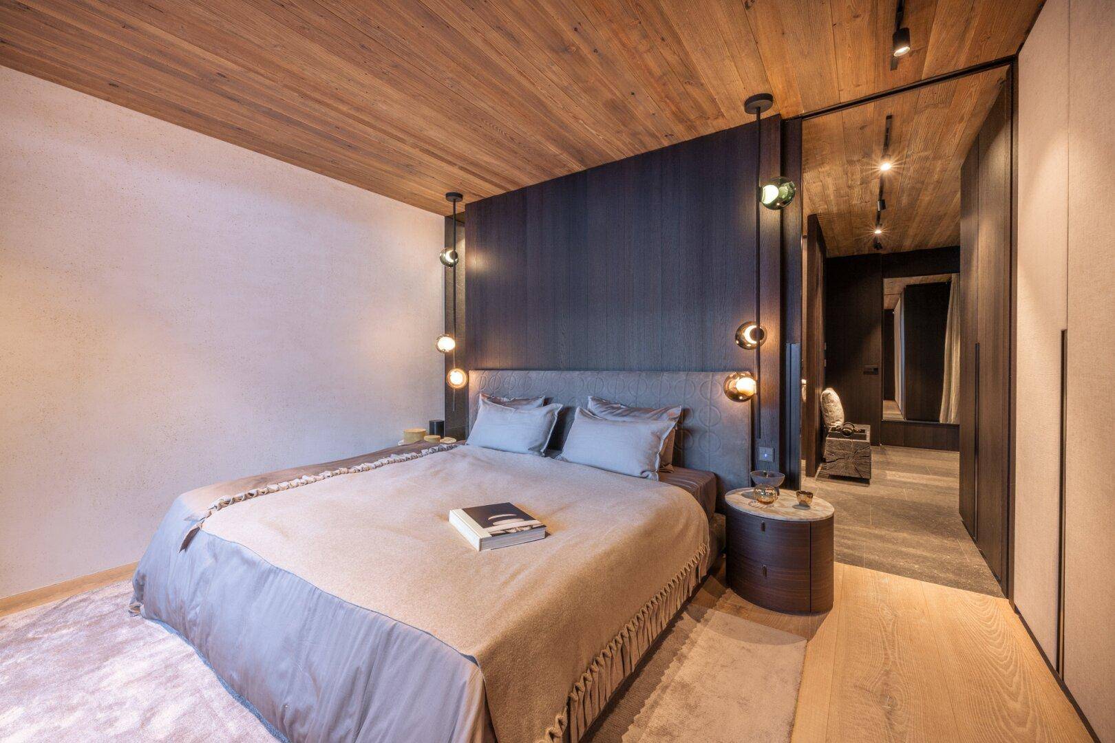 Gemütliches Schlafzimmer mit Holzbalkendecke, dunkler Akzentwand und indirekter Beleuchtung.