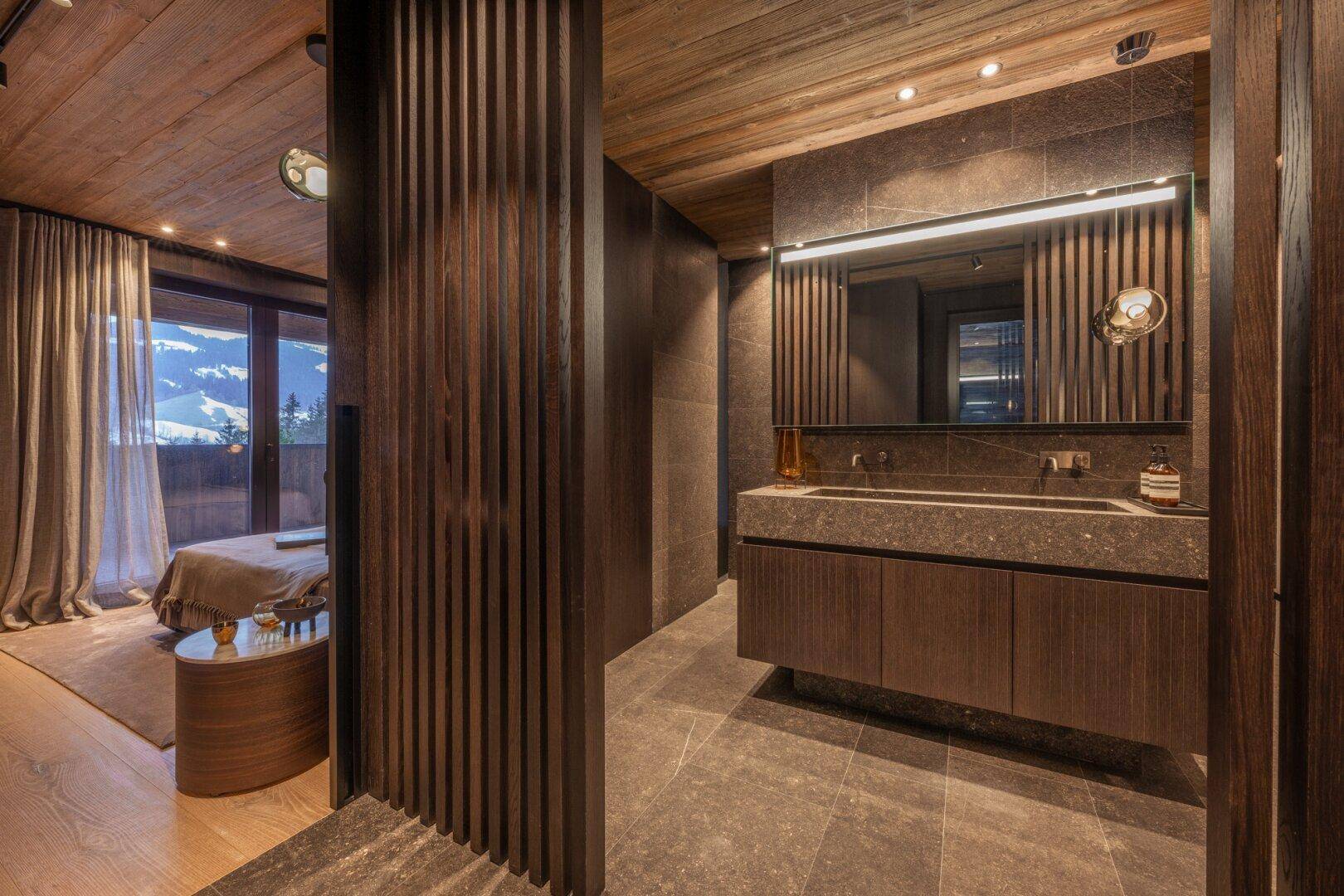 Elegantes Badezimmer mit Doppelwaschbecken, dunklen Oberflächen und Holzakzenten, angrenzend an das Schlafzimmer.
