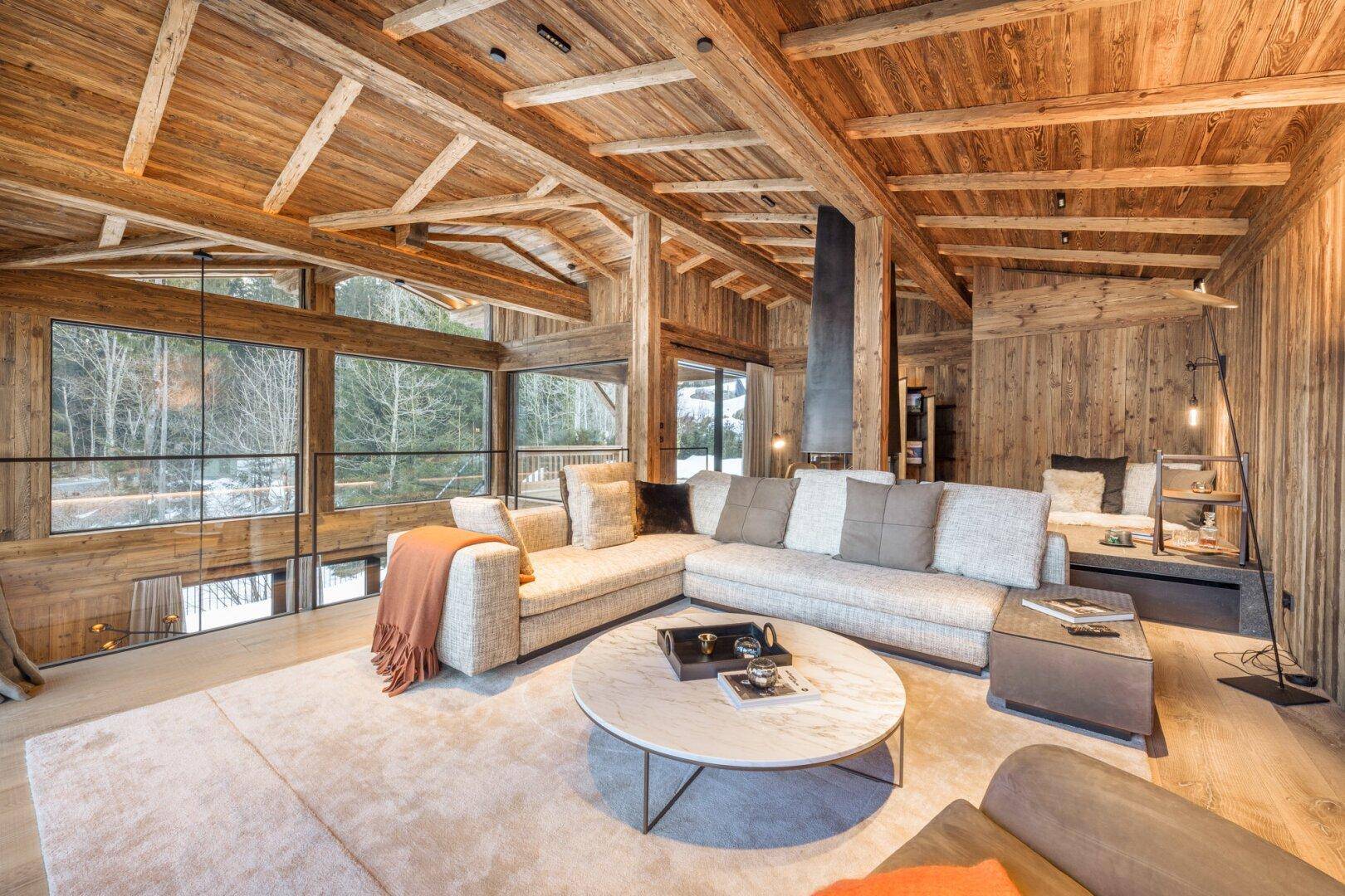 Helles Wohnzimmer mit bequemer Sitzecke, Holzwänden und -decken sowie weitem Blick in die Natur.