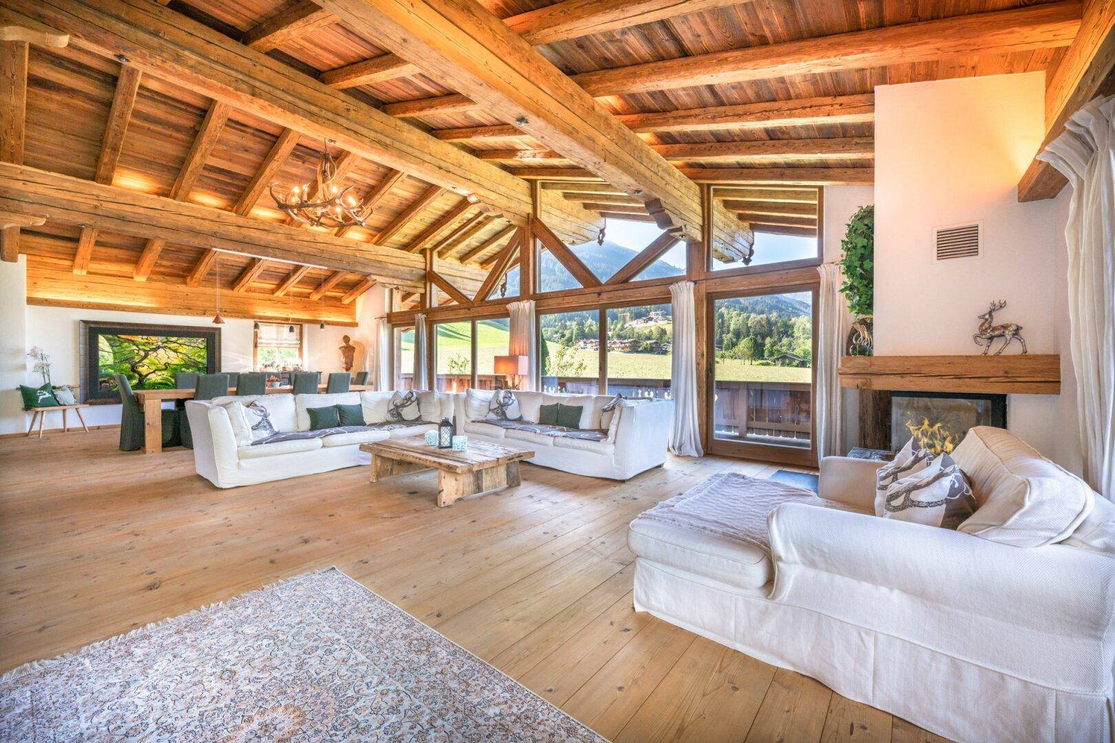 Heller Wohnbereich mit Holzboden, Kamin und großen Fenstern, die einen weiten Blick bieten.
