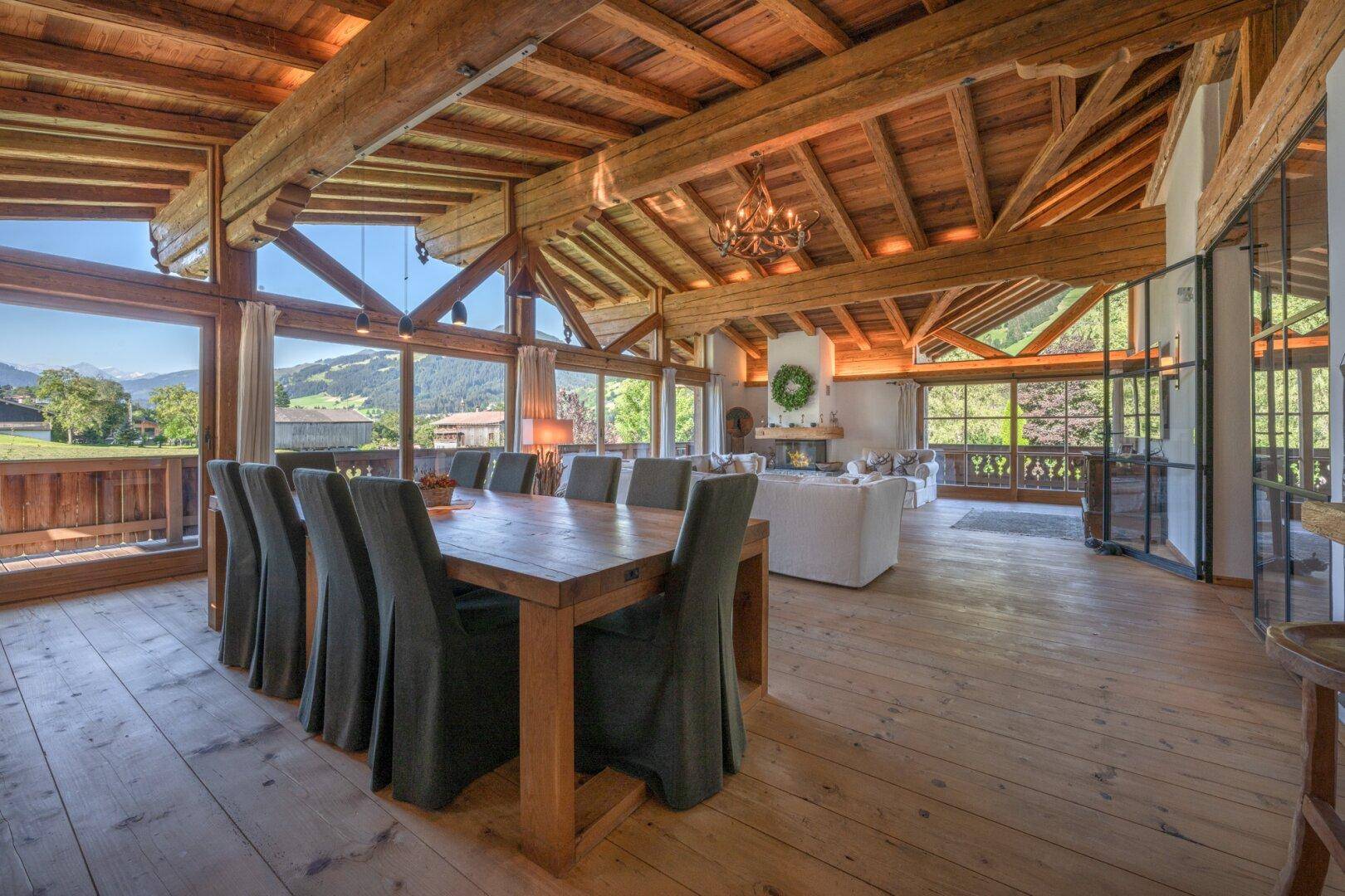Essbereich mit großem Holztisch und Stühlen, umgeben von Panoramafenstern mit Bergblick.