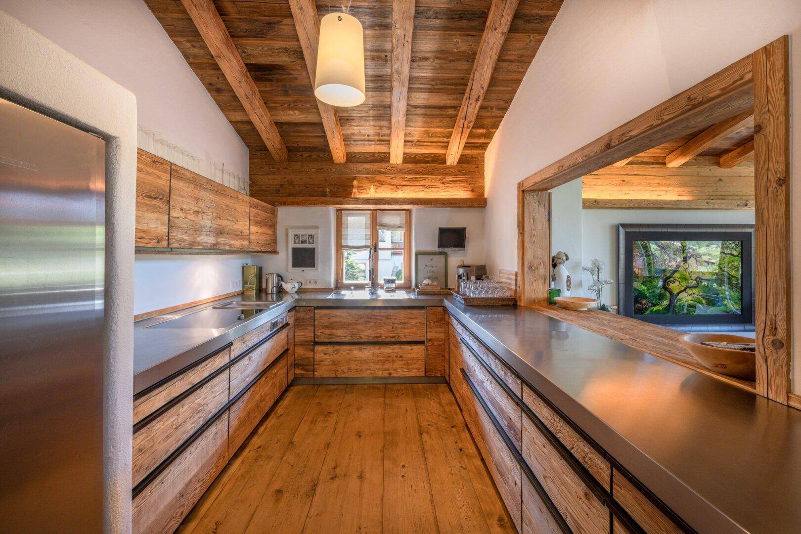 Rustikale Holzküche mit Edelstahl-Arbeitsplatten und Holzbalkendecke im Landhausstil.