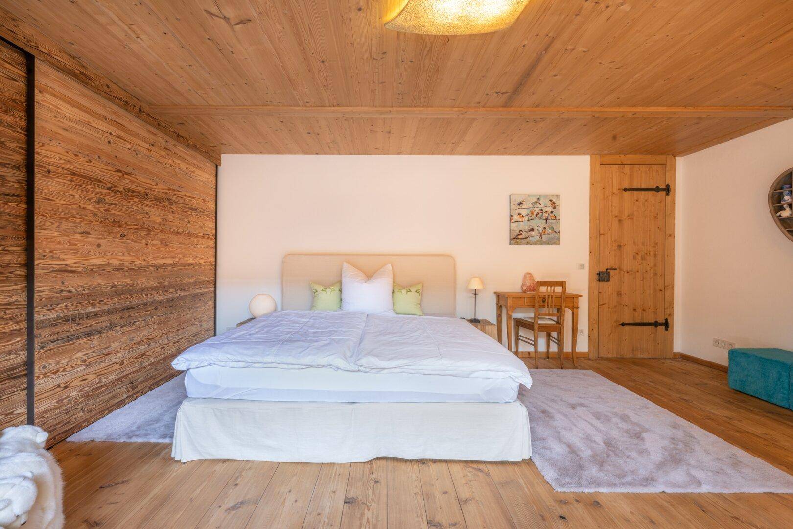 Schlafzimmer mit Holzwänden, Holzboden und einem großen Doppelbett in ruhiger Atmosphäre.