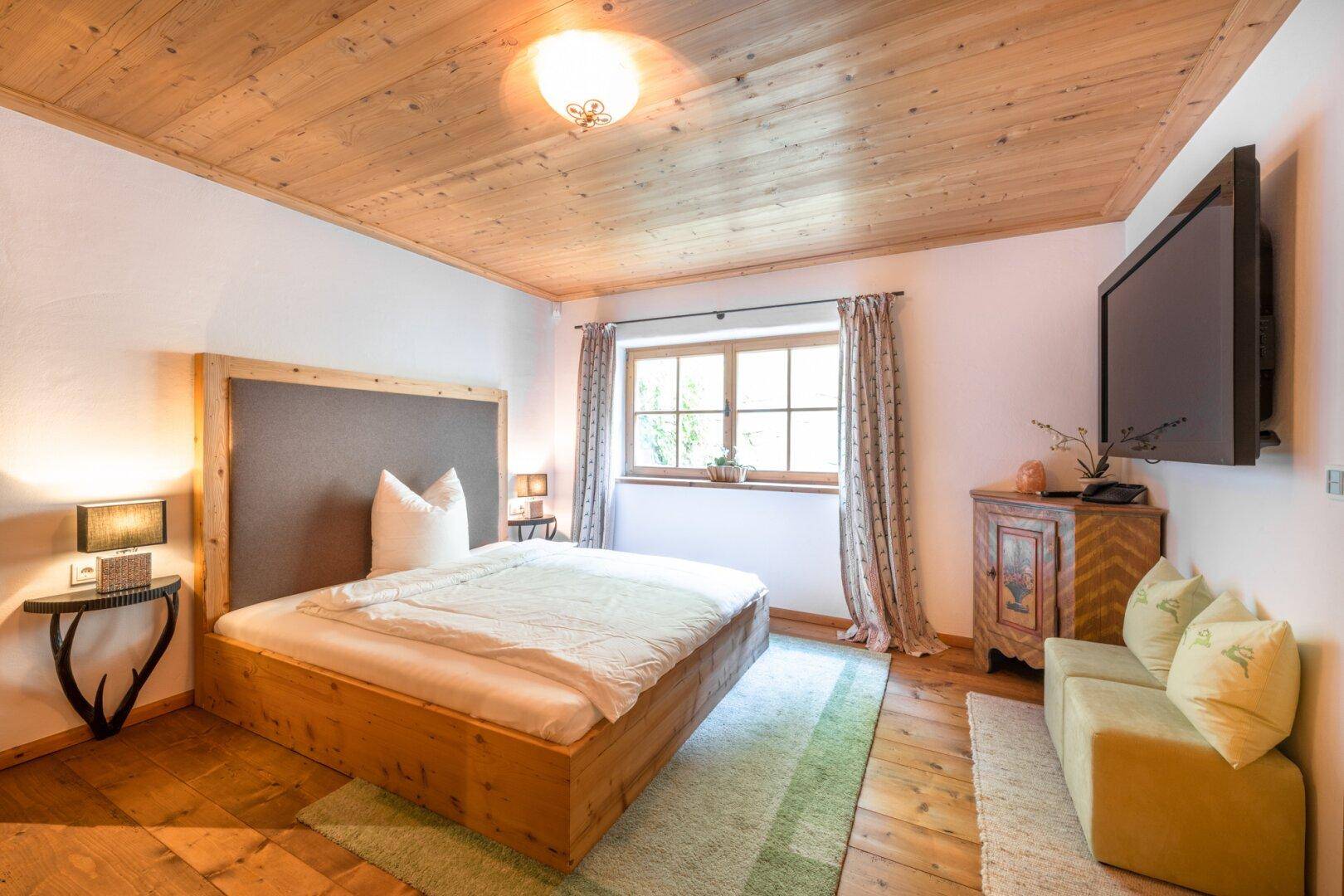 Helles Schlafzimmer mit Holzboden, Holzbett und Fenster mit Blick ins Grüne.