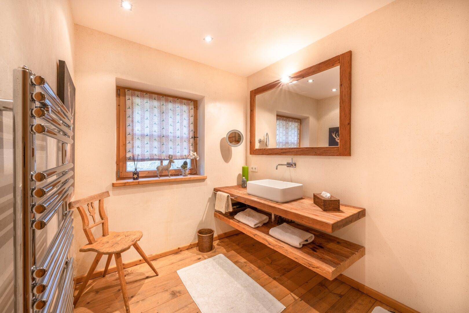 Kleines Badezimmer mit Einzelwaschbecken, Holzmöbeln und beheiztem Handtuchhalter.