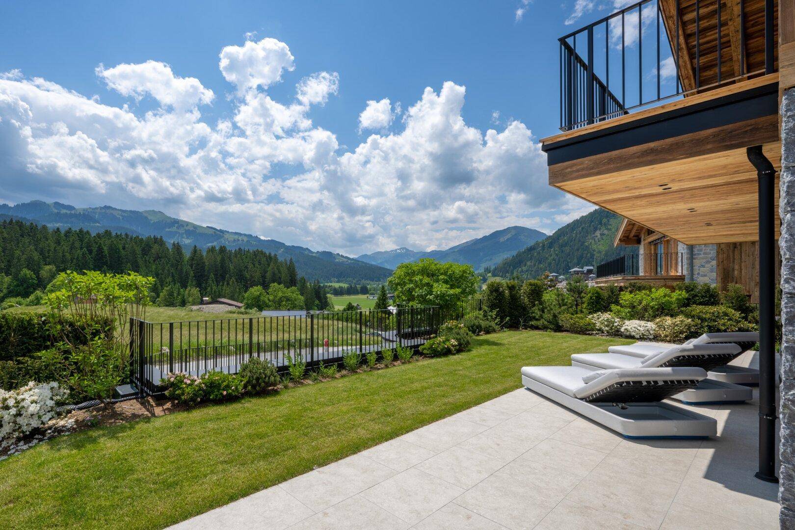 Gepflegter Gartenbereich mit Liegestühlen und Terrasse, umgeben von grüner Natur und Bergen.