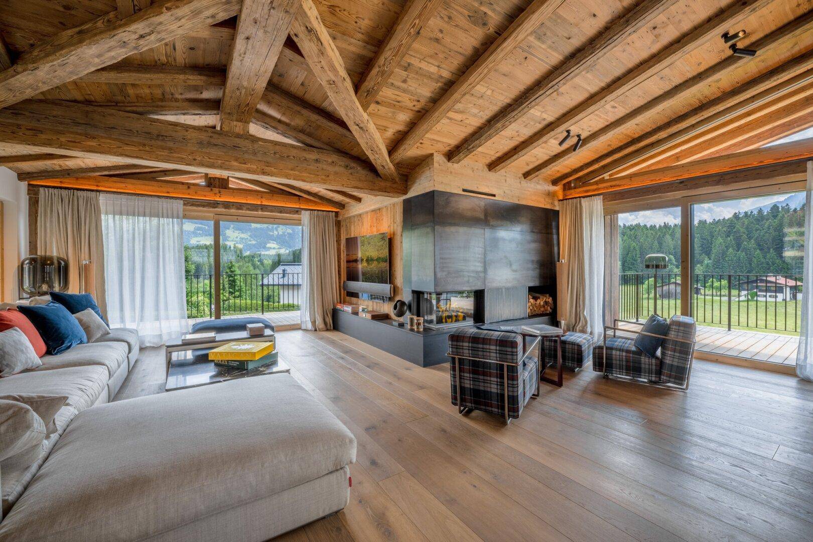 Gemütliches Wohnzimmer mit Holzbalkendecke, Kamin und großen Fenstern mit Bergblick.
