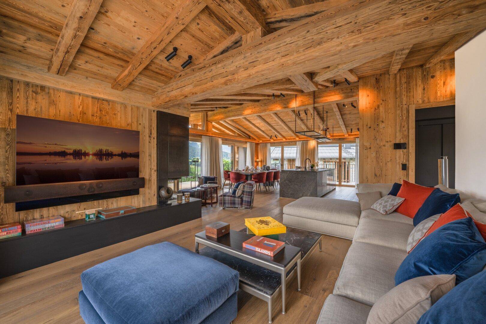 Offener Wohnbereich mit Holzwänden, großem Fernseher und Blick auf den Ess- und Küchenbereich.