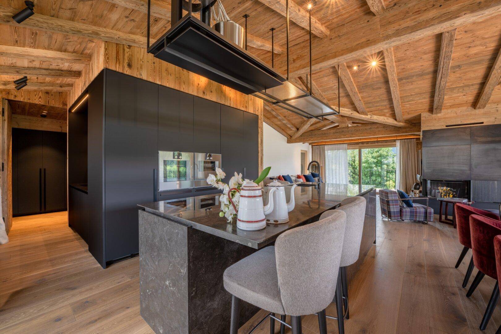 Moderne schwarze Küche mit Kochinsel, Barhockern und Holzbalkendecke im offenen Wohnbereich.