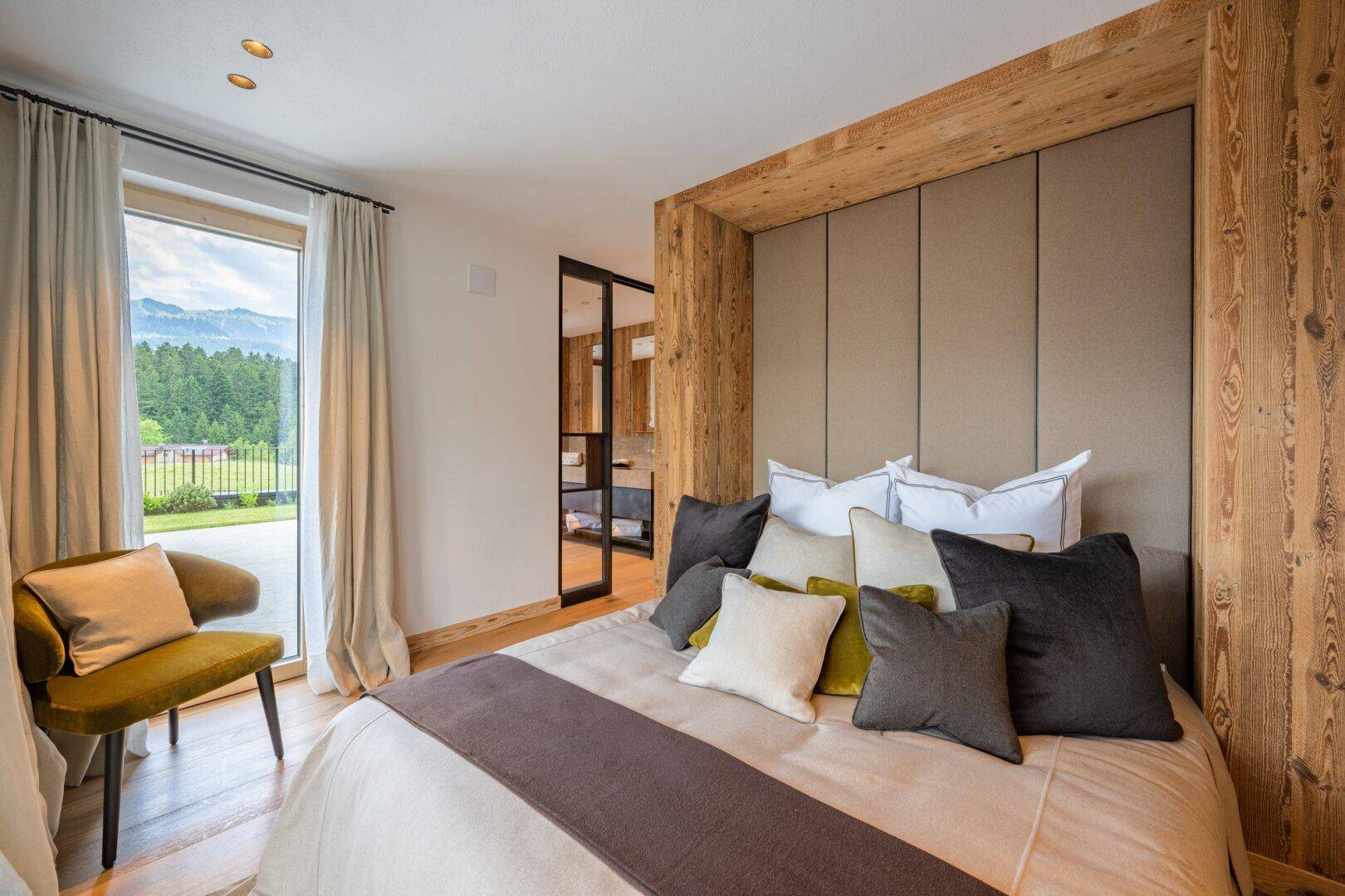 Helles Schlafzimmer mit Holzakzenten, großem Bett und Blick auf die Berge durch die Terrassentür.