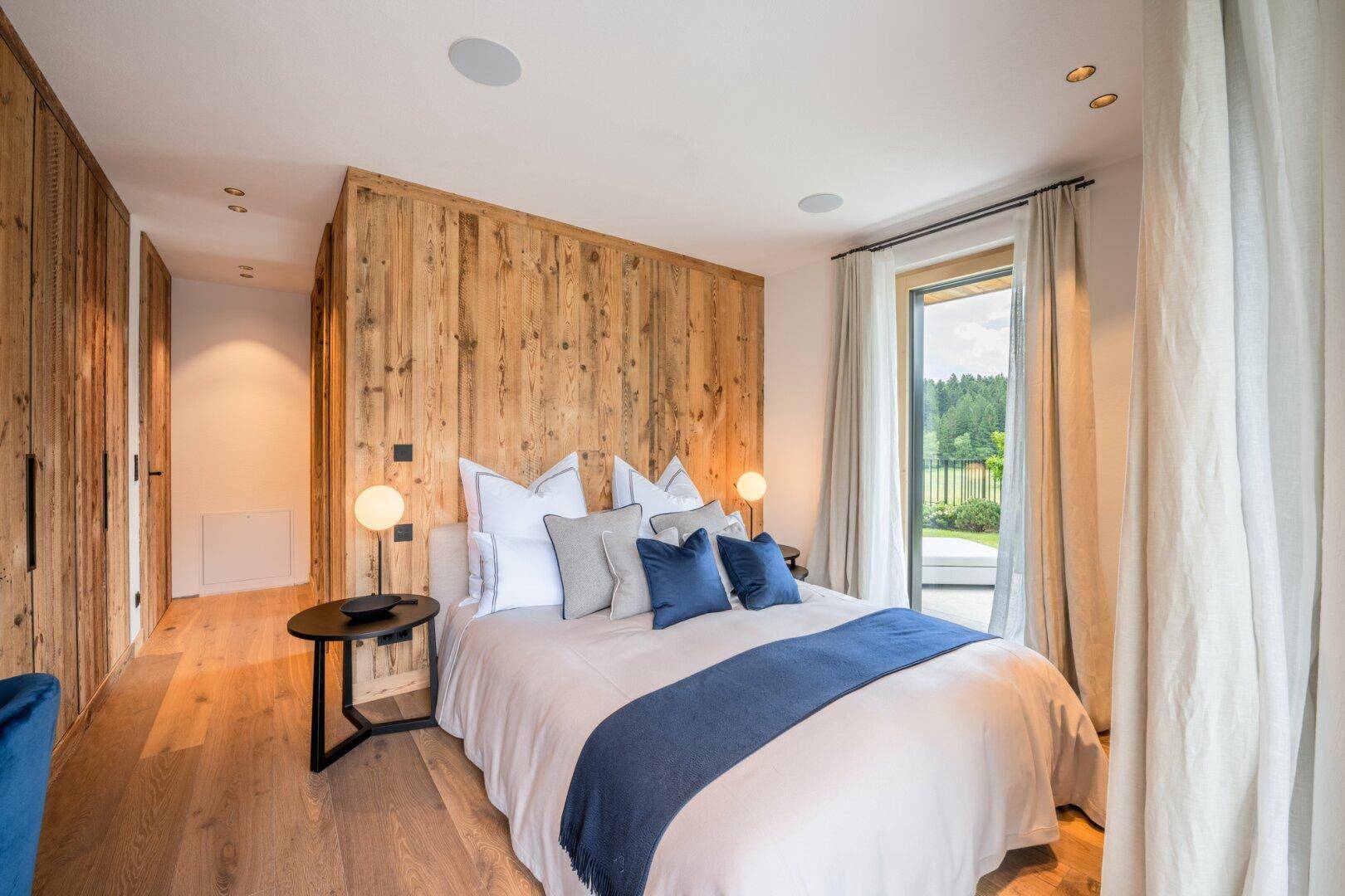 Stilvolles Schlafzimmer mit Holzwänden, großem Bett und Zugang zu einem Außenbereich.