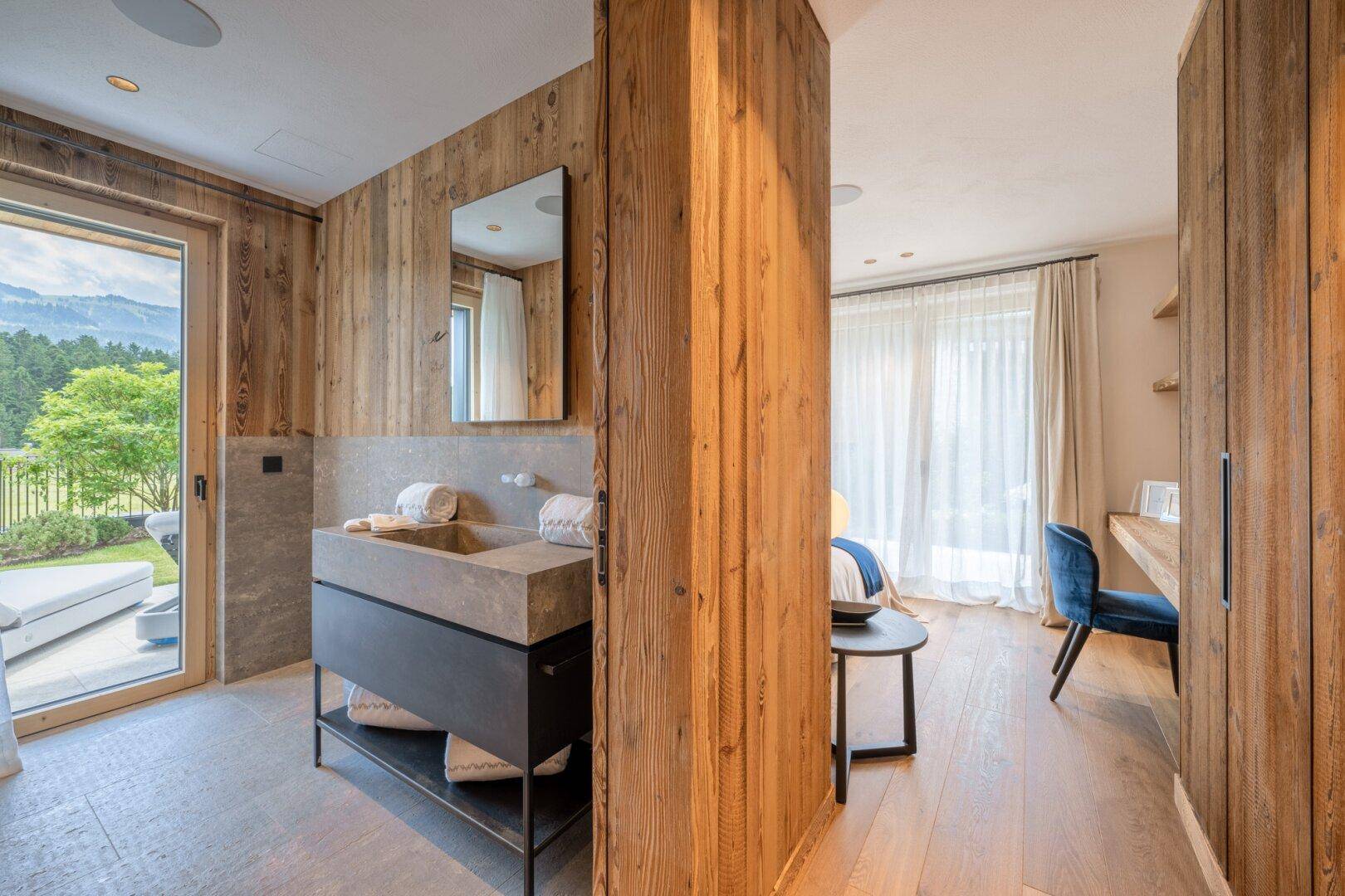 Offenes Badezimmer mit Steinwaschbecken und Holzwänden, verbunden mit einem Schlafzimmerbereich.