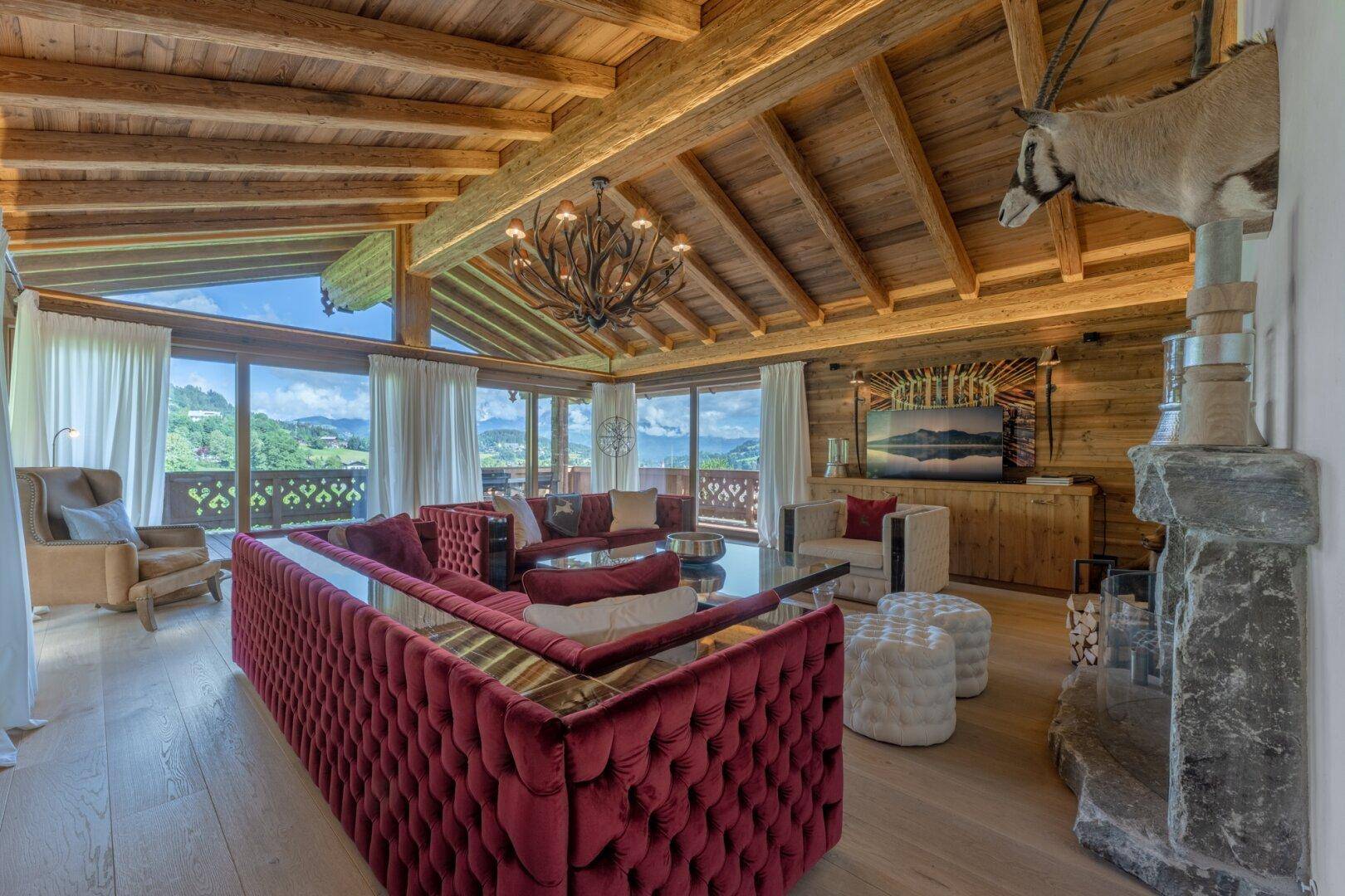 Geräumiges Wohnzimmer im alpinen Stil mit Holzbalkendecke, Kamin und Panoramablick auf die Berge.