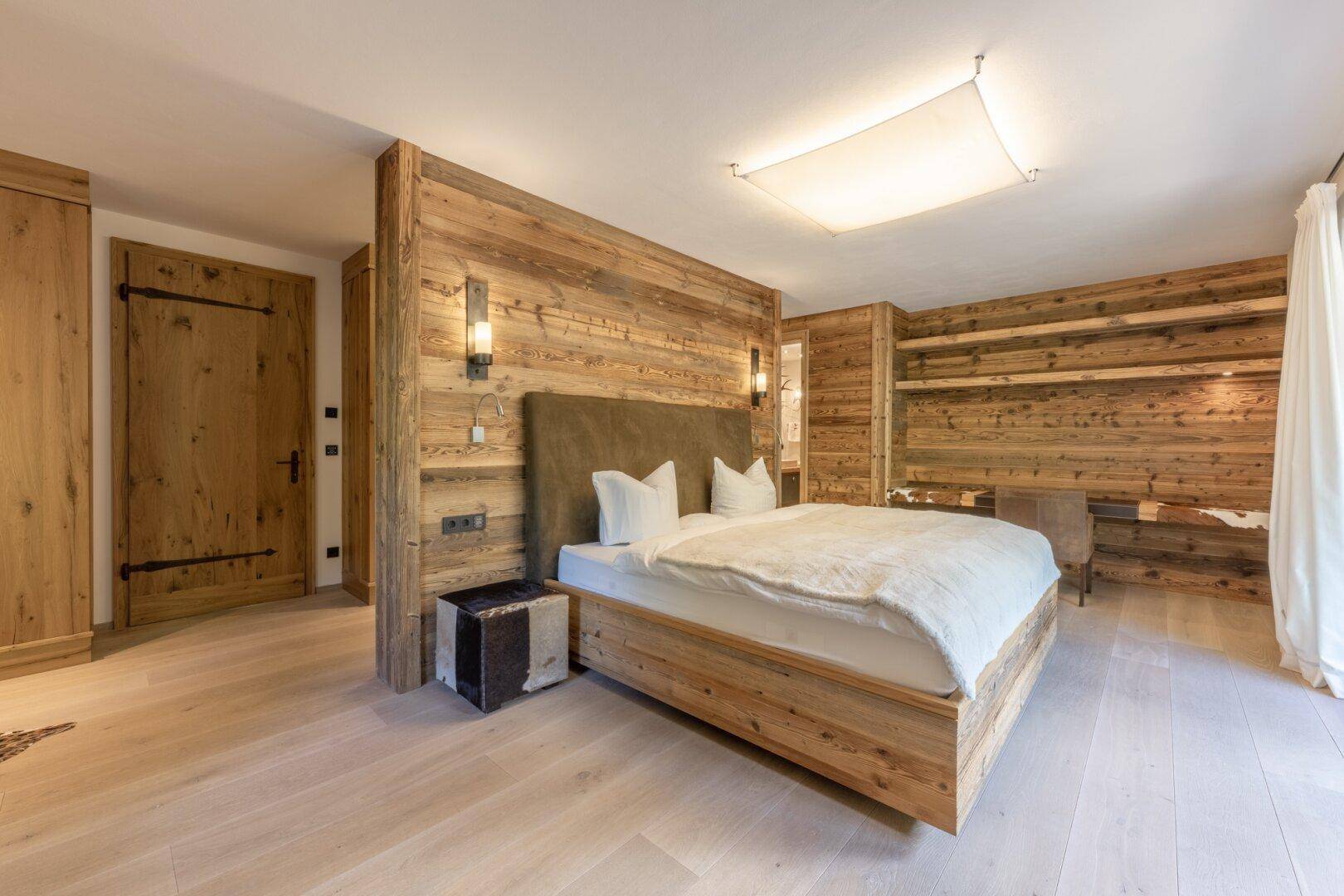 Gemütliches Schlafzimmer mit Holzwänden, hellem Holzboden und modernem Bett.