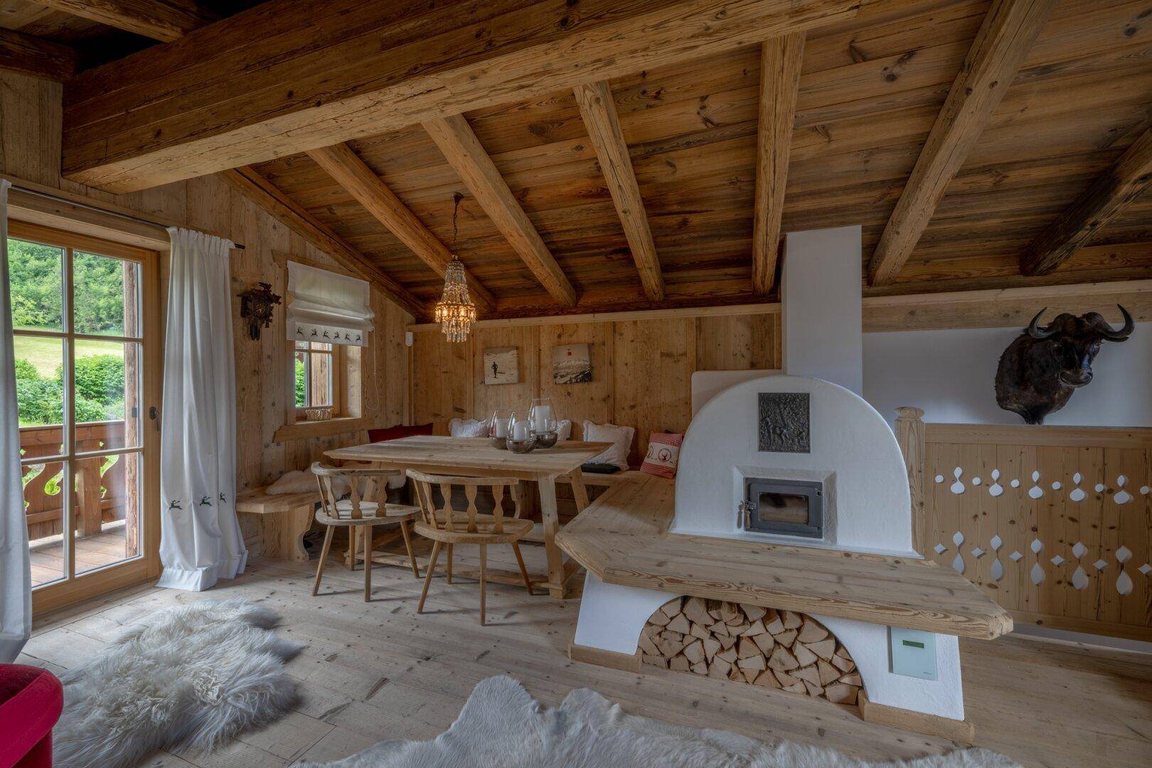 Gemütlicher Essbereich im Landhausstil mit Kachelofen, Holzbalkendecke und Zugang zum Balkon.
