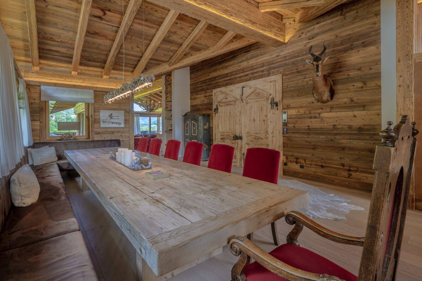 Rustikaler Essbereich mit großem Holztisch, Holzbalkendecke und traditionellen roten Stühlen.