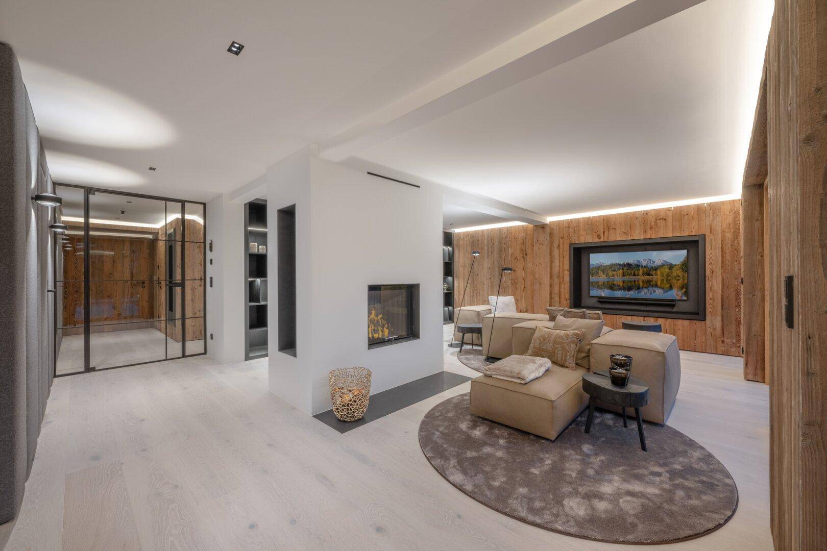 Helles Wohnzimmer mit modernem Kamin, Holzwänden und einer eleganten Glasabtrennung zu einem weiteren Raum.