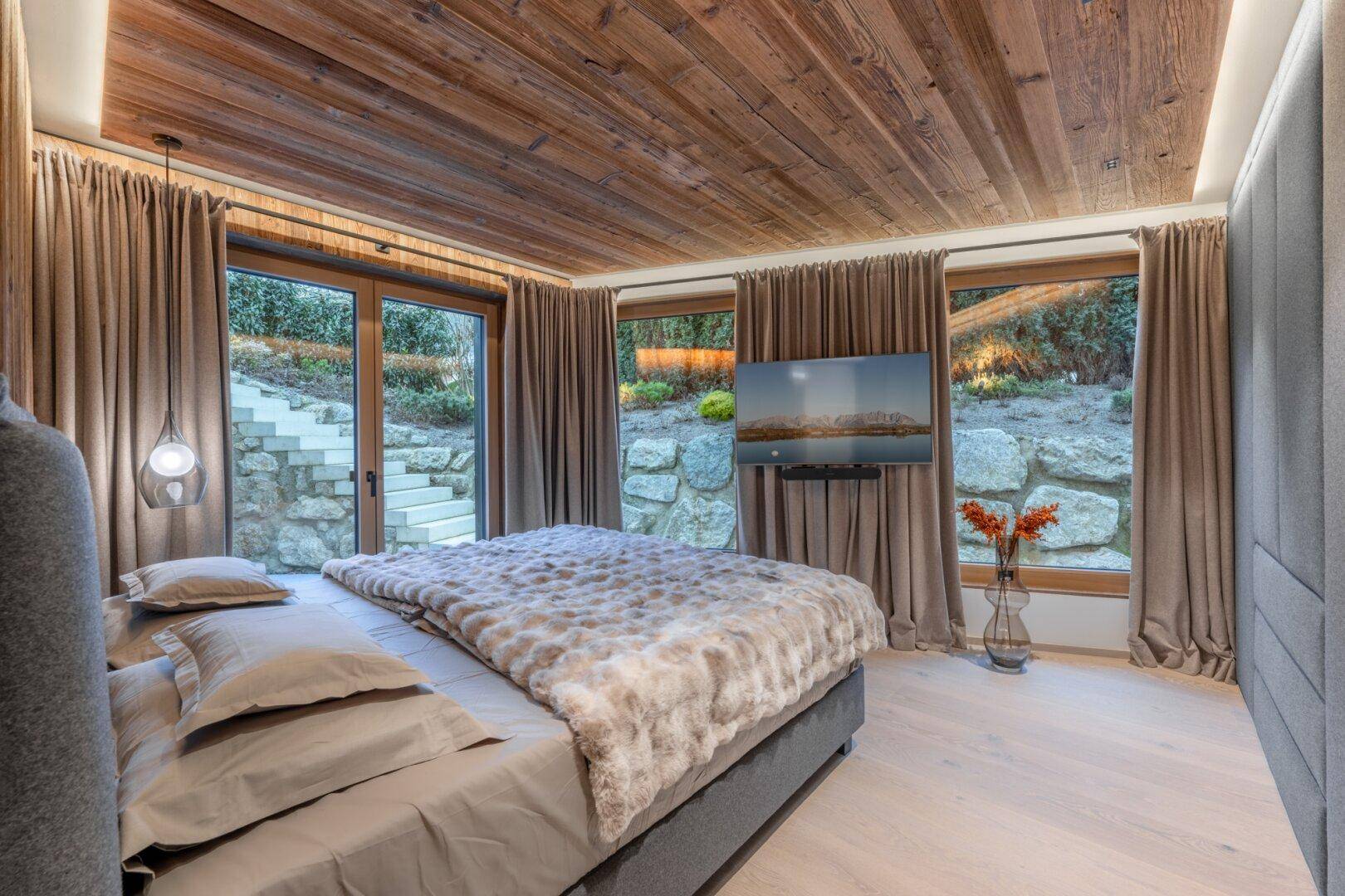 Schlafzimmer mit großem Bett, Holzwänden und direktem Zugang zu einem felsigen Gartenbereich.