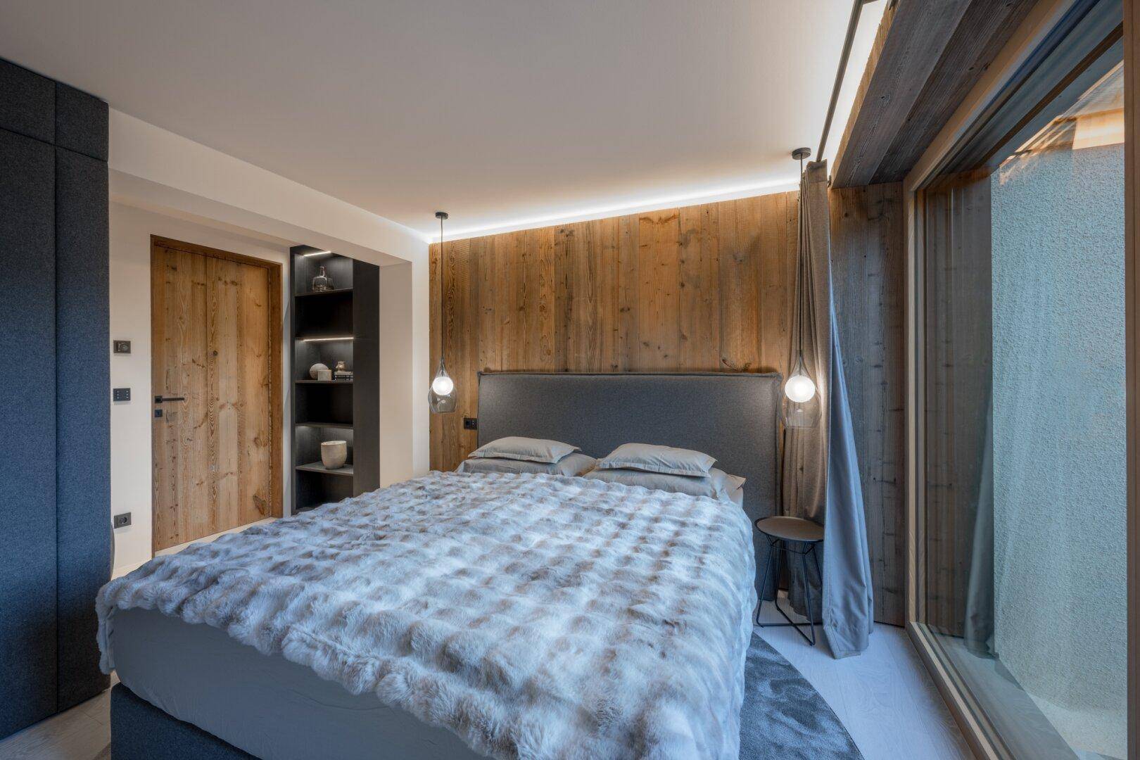 Gemütliches Schlafzimmer mit Holzwand, großem Bett und bodentiefen Fenstern für viel Tageslicht.