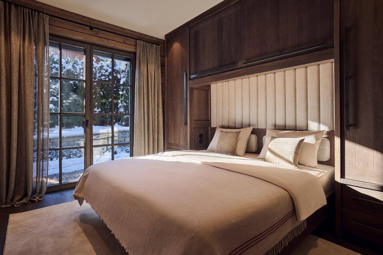 Elegantes Schlafzimmer mit großem Bett, integrierten Holzschränken und großen Fenstern mit Blick auf die Natur.
