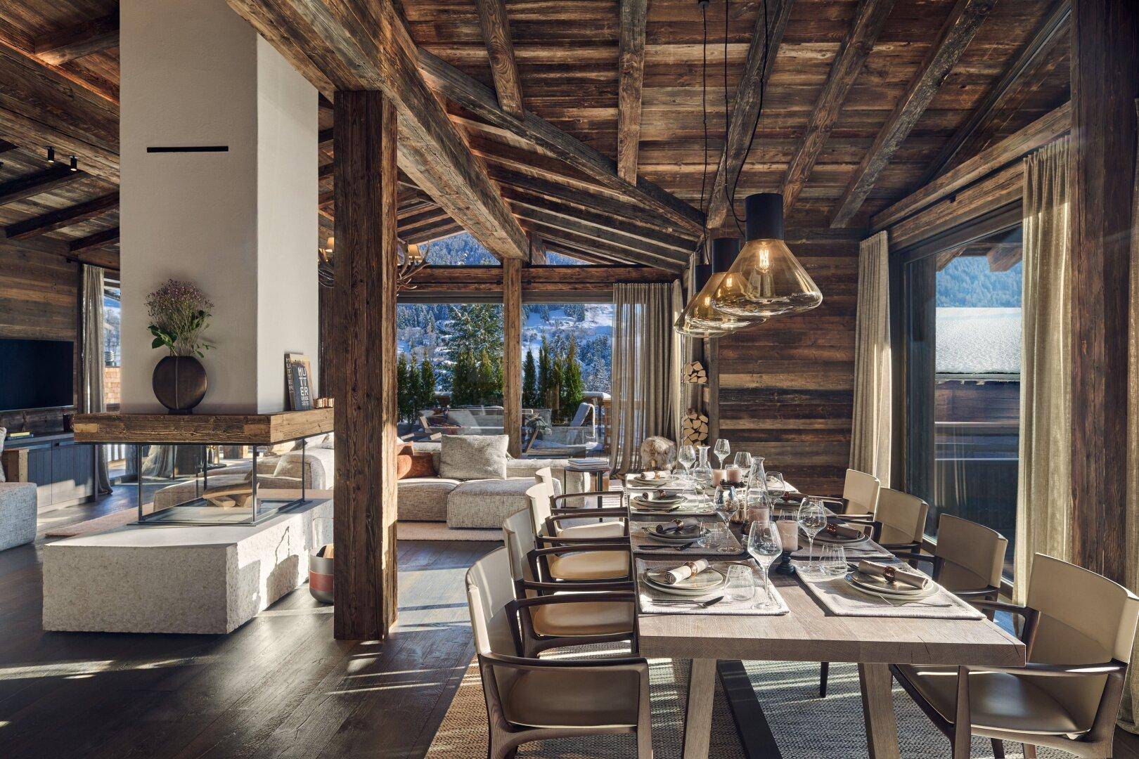 Eleganter Essbereich mit Holztisch, Kamin und großen Fenstern, die einen malerischen Bergblick bieten.