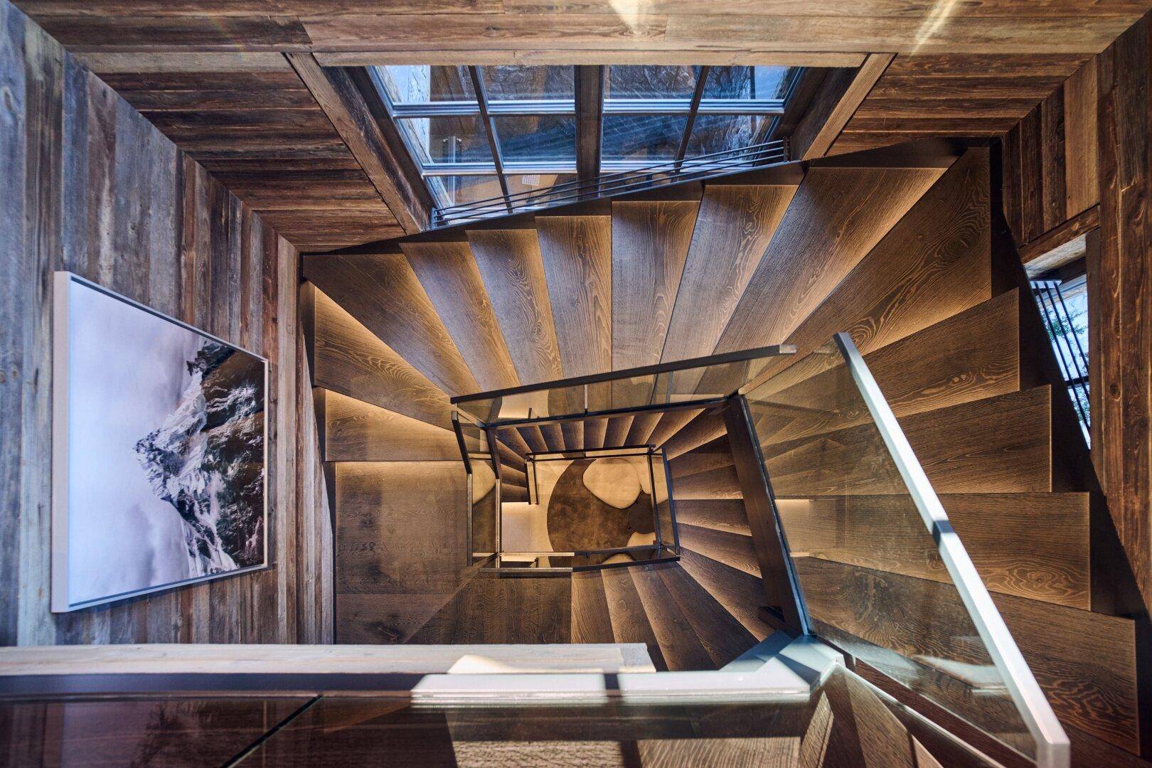 Elegante Holztreppe mit Glasgeländer und integrierter Beleuchtung, die von einem Oberlicht erhellt wird.