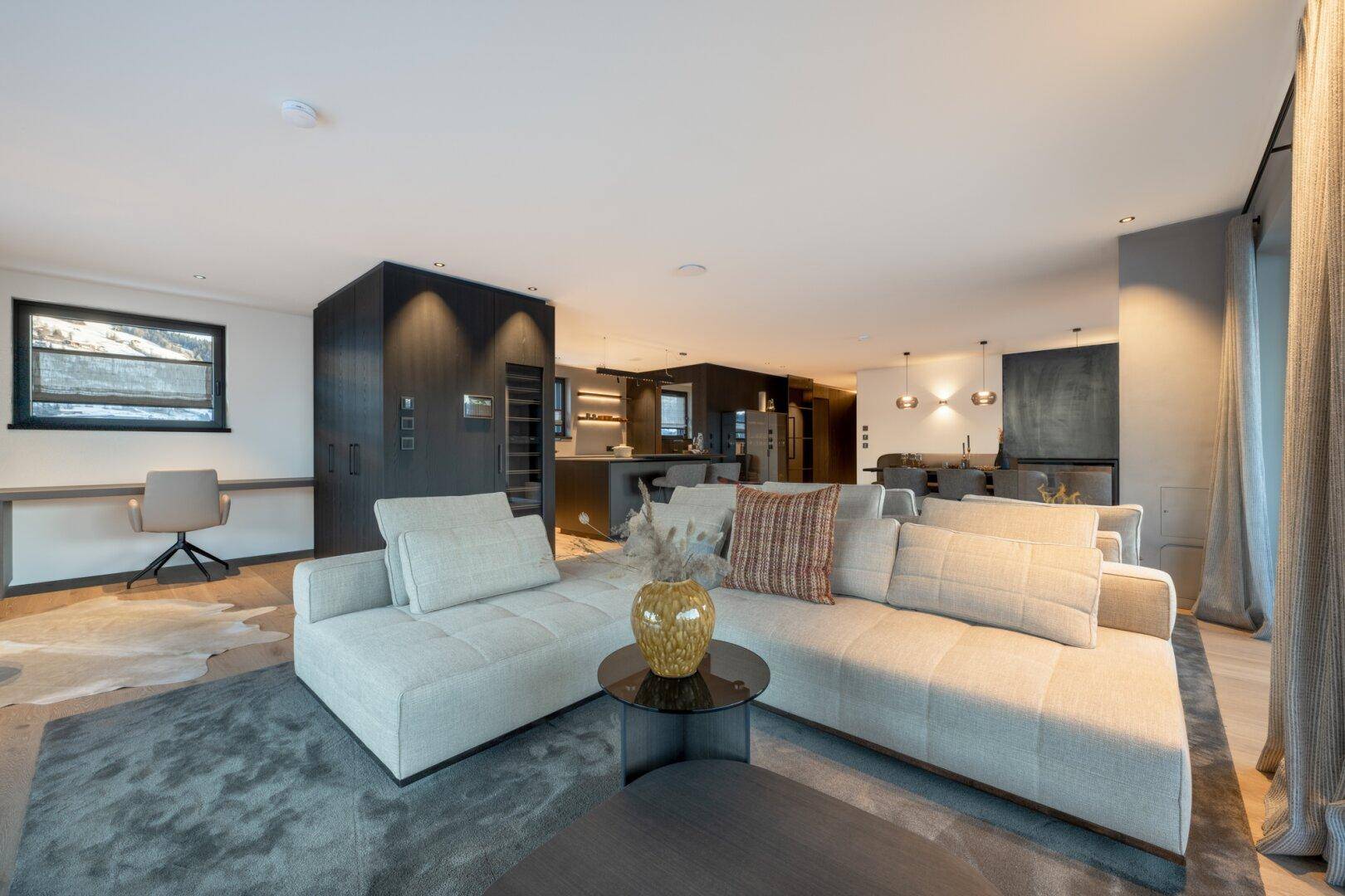 Moderner Wohnbereich mit bequemen Sofas, integriertem Arbeitsplatz und Blick in den Küchenbereich.