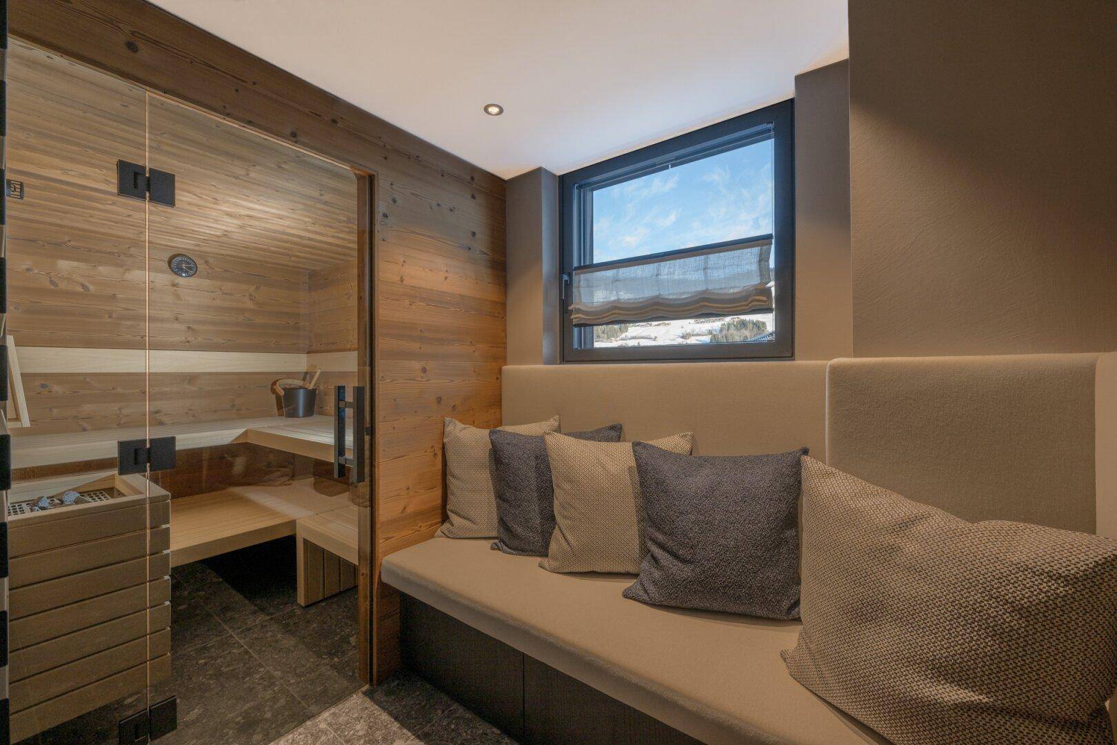 Entspannungsbereich mit Sauna, bequemer Sitzbank und Fensterblick auf die verschneite Landschaft.