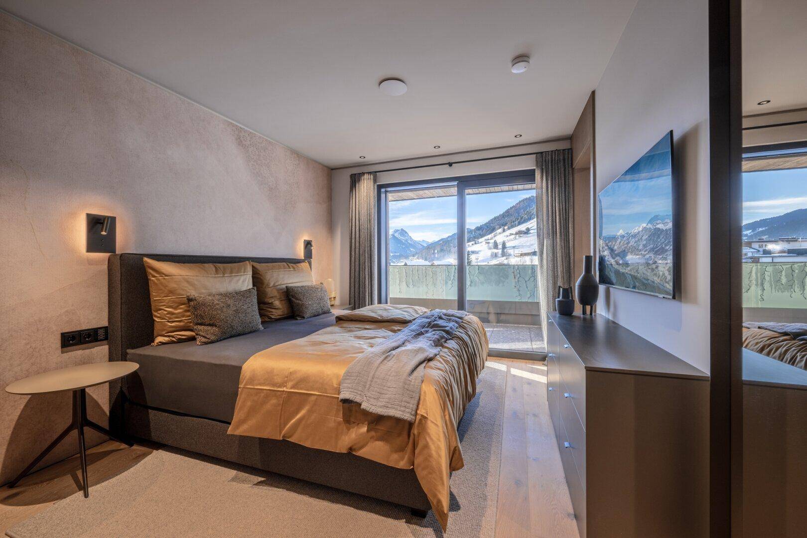 Gemütliches Schlafzimmer mit Doppelbett, Holzboden und direktem Zugang zum Balkon mit Bergblick.