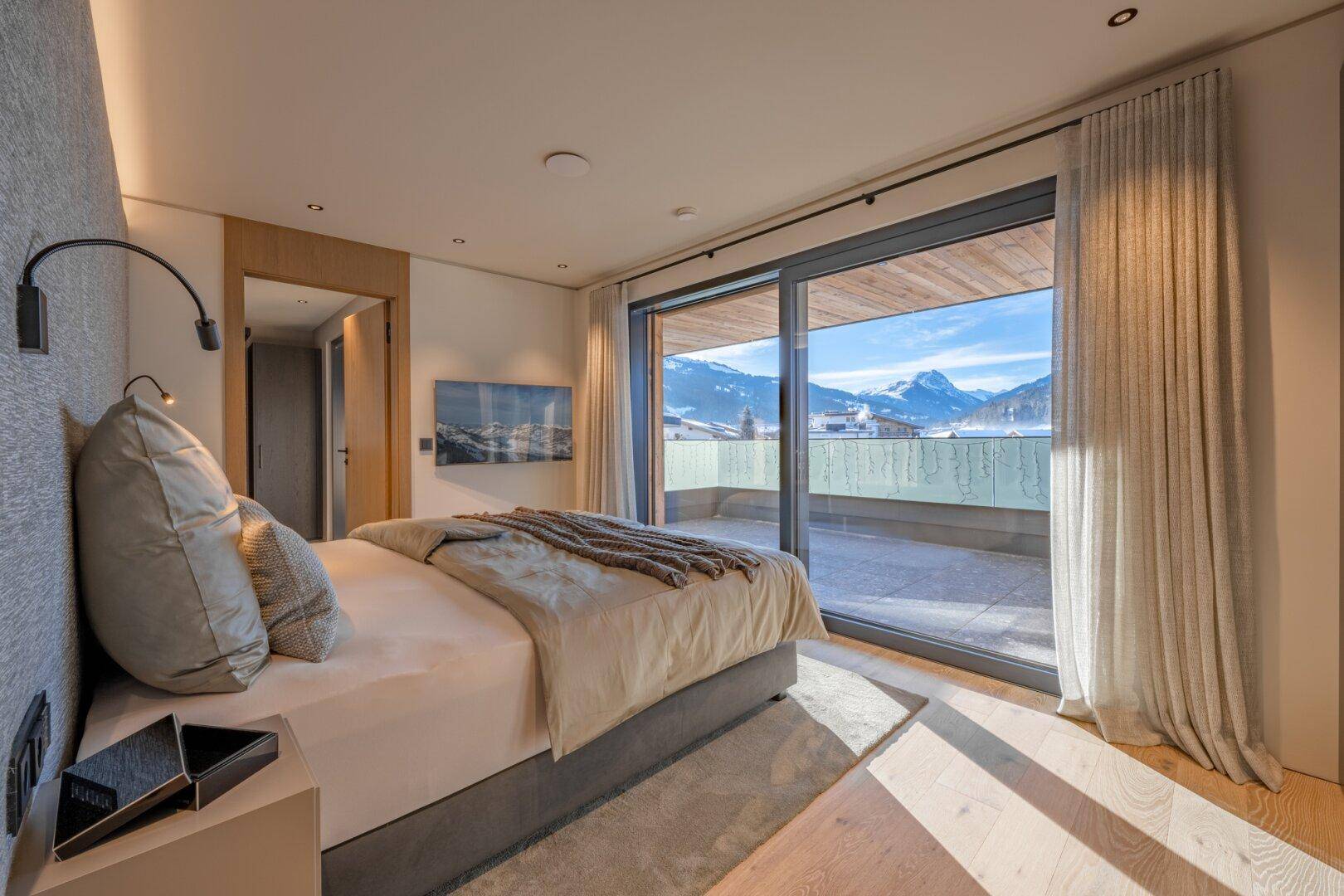 Geräumiges Schlafzimmer mit bequemen Bett, Holzboden und Panoramablick auf die verschneite Berglandschaft.