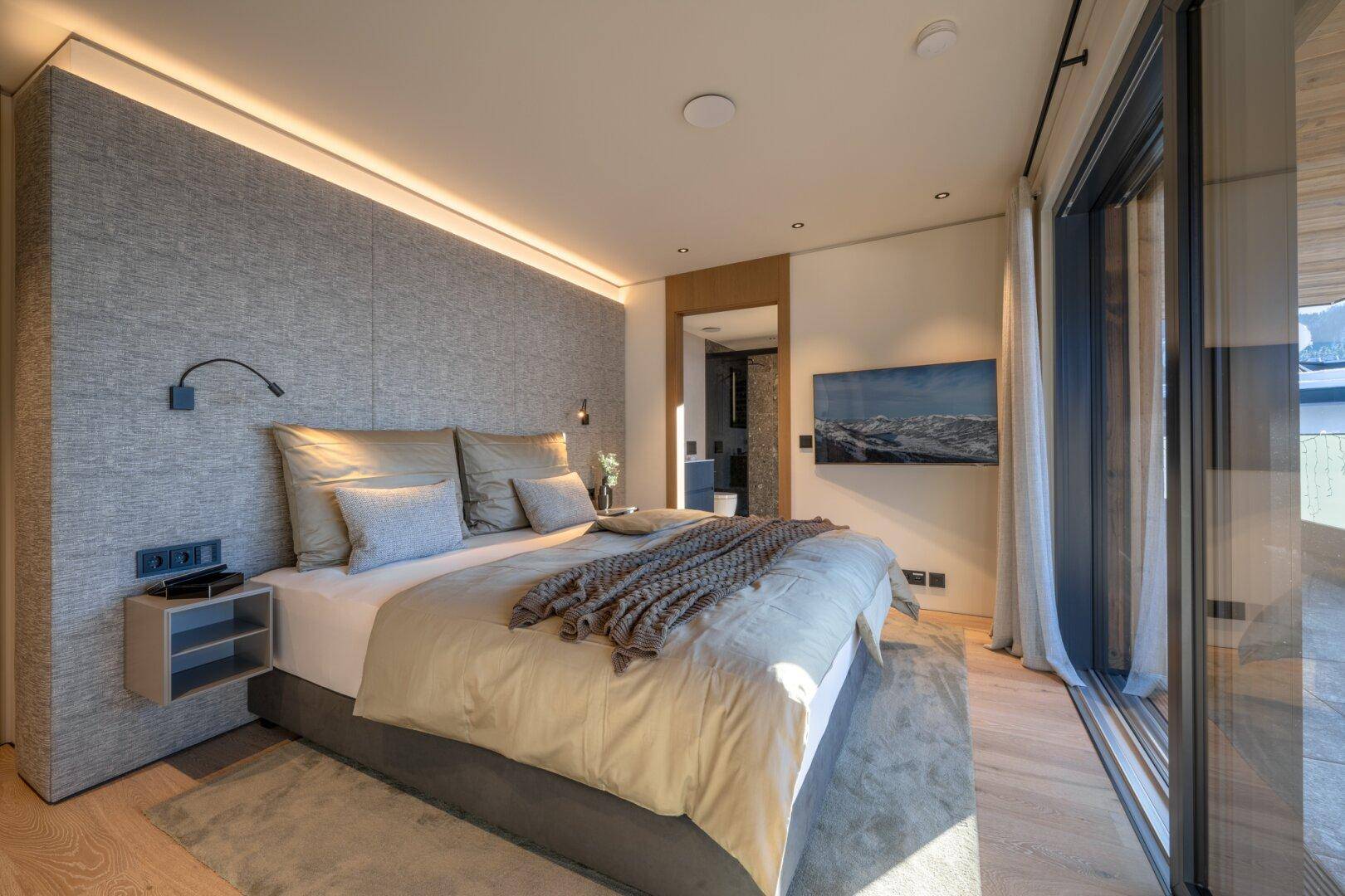 Helles Schlafzimmer mit großem Bett, Holzboden und Zugang zu einem Balkon mit Bergblick.