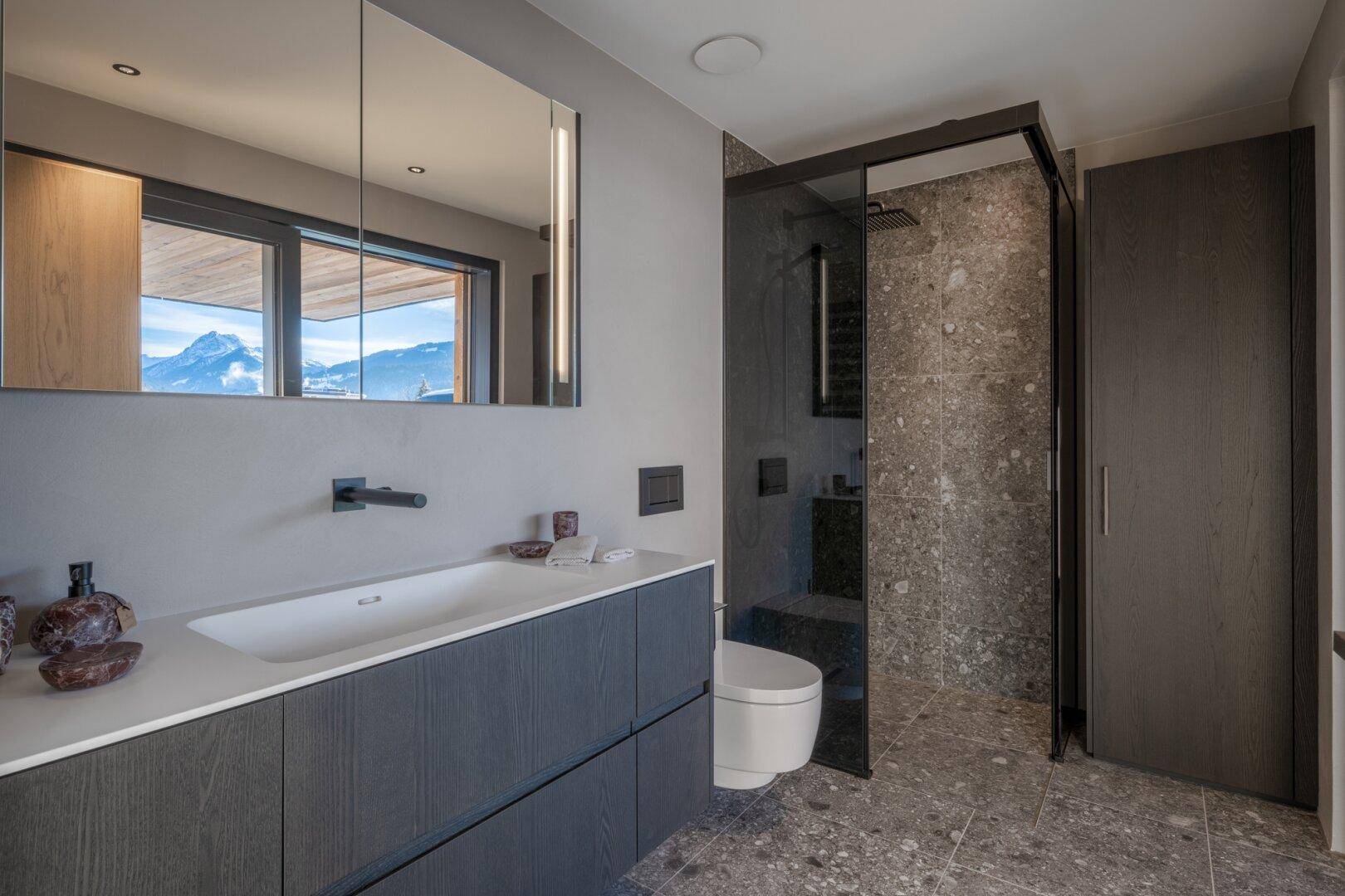 Modernes Badezimmer mit begehbarer Dusche, Wand-WC und eleganten grauen Fliesen.