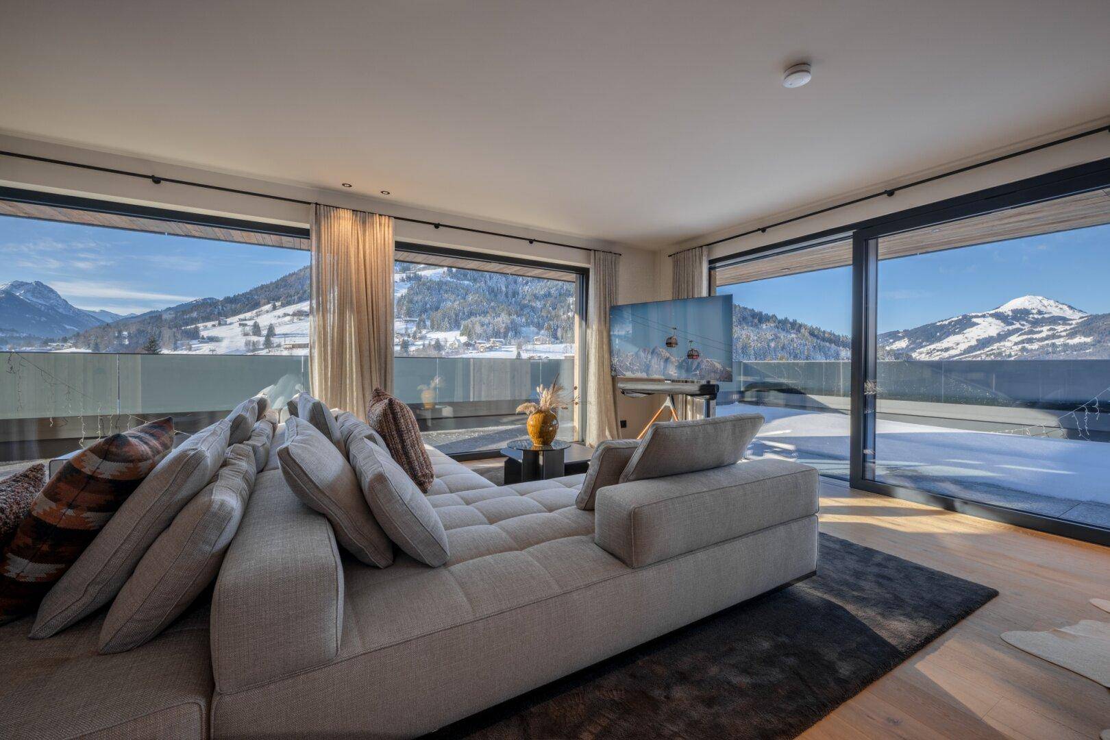 Geräumiges Wohnzimmer mit moderner Einrichtung, großen Fenstern und Panoramablick auf die verschneiten Berge.