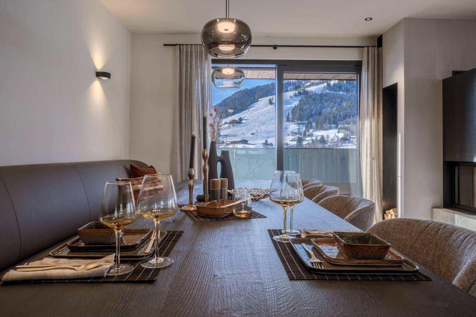 Gemütlicher Essbereich mit Holztisch, moderner Dekoration und Blick auf die verschneiten Berge.